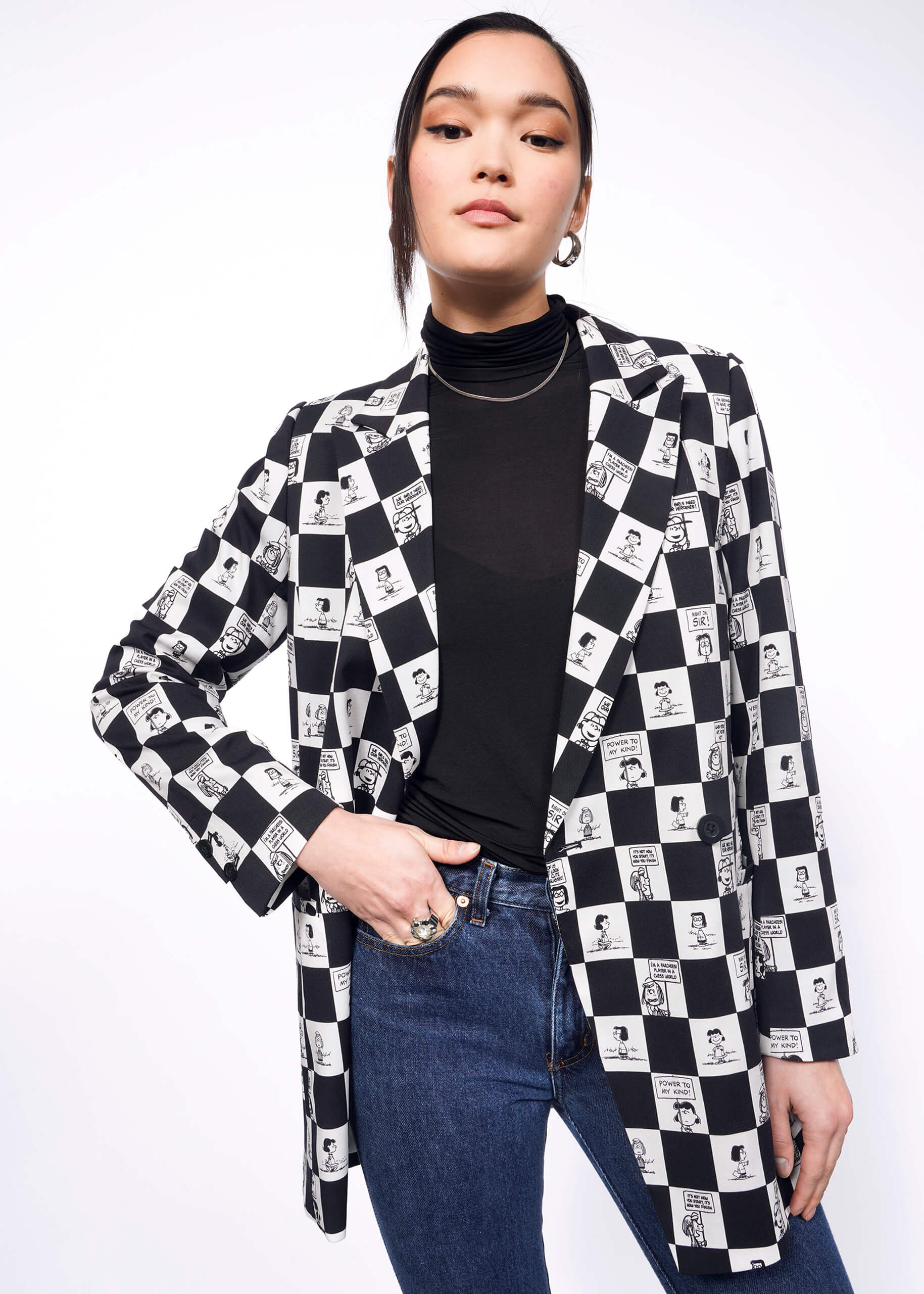 S=Model with black hair tied back wears a black turtleneck, jeans, and Person with long black hair wears The Peanuts x Wildfang Double Breasted Blazer in a custom black and white checkered print featuring Peanuts characters.