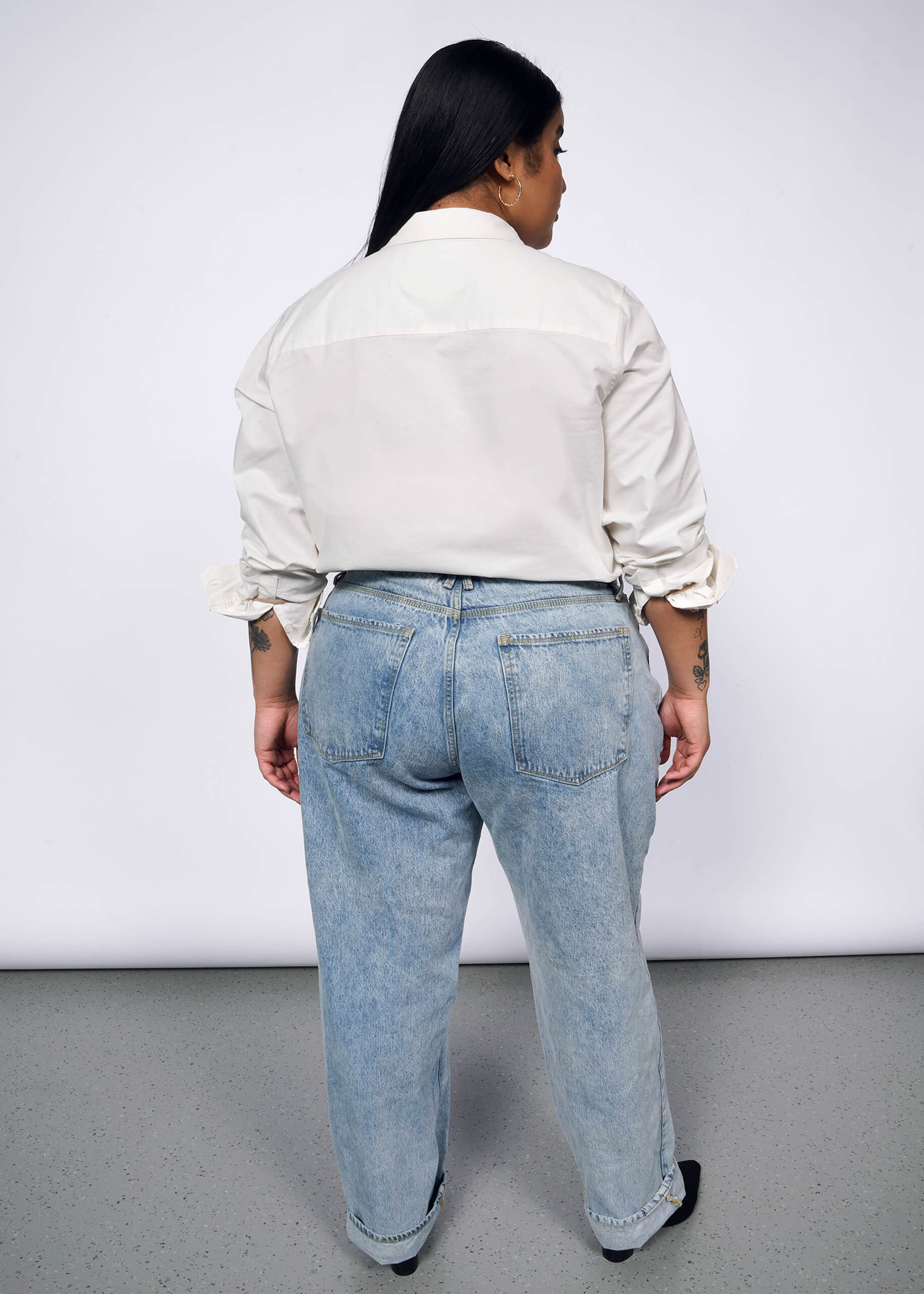 1X=Back view of person with long black hair wearing The Peanuts x Wildfang Long Sleeve Button Up shirt and jeans.
