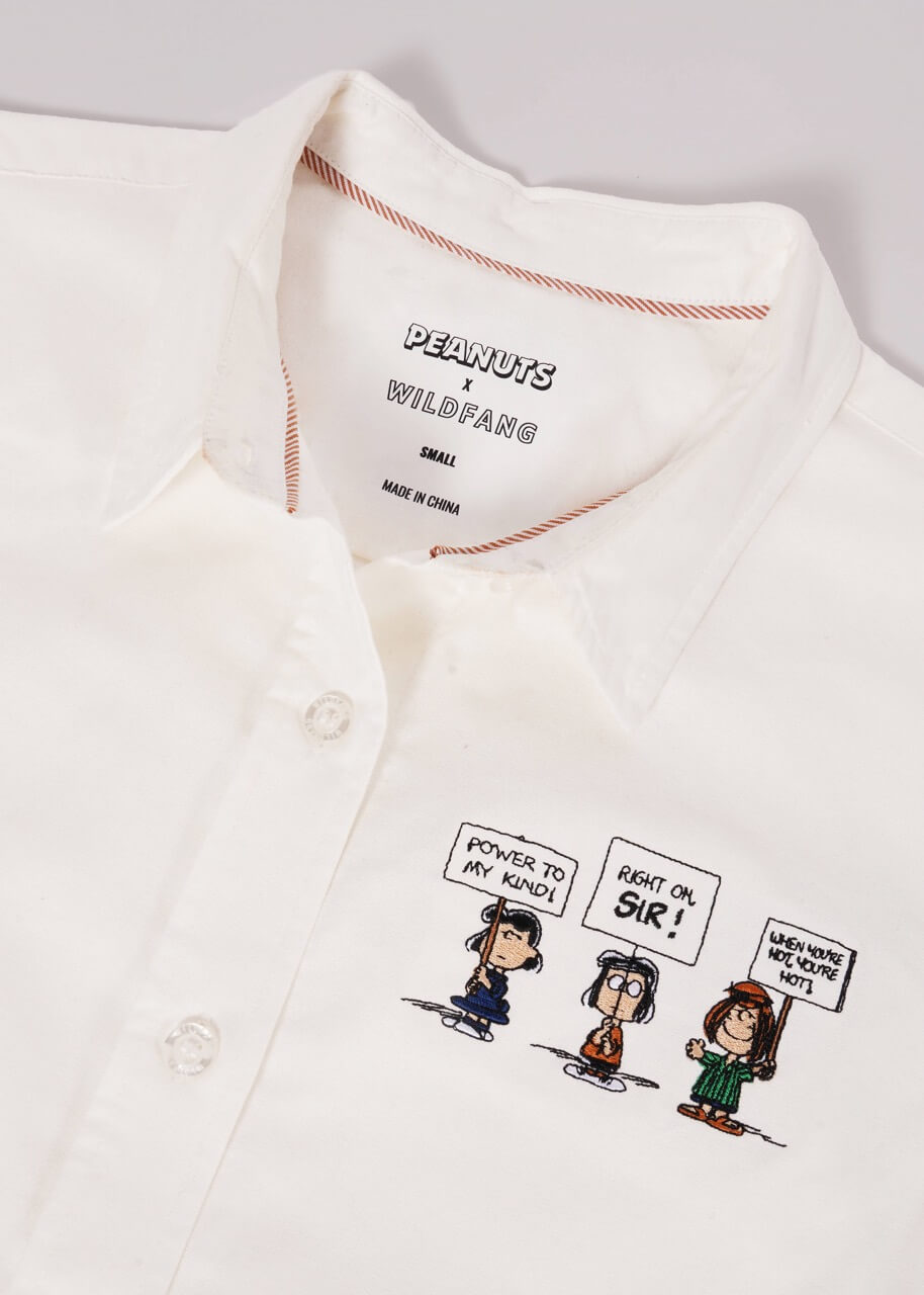 The Peanuts x Wildfang Long Sleeve Button Up laying flat on white background showing Peanuts x Wildfang logo on inside of shirt and details of embroidered Peanuts characters.