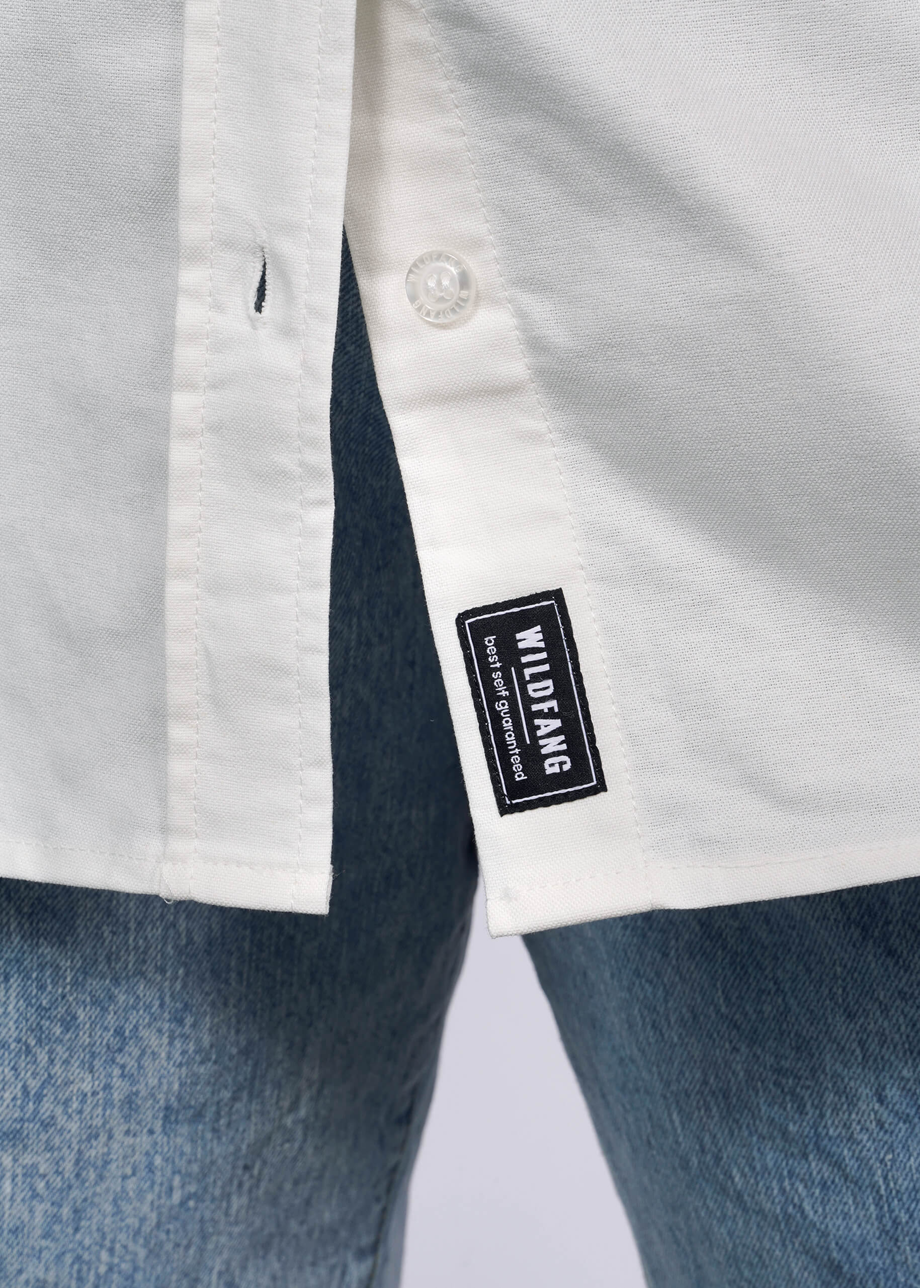 S=Close up of bottom hem of The Peanuts x Wildfang Long Sleeve Button Up showing WILDFANG tag.