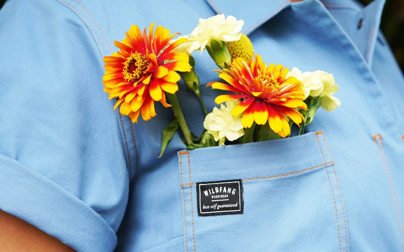 Close up of blue coverall pocket with orange and red flowers sticking out of pocket.
