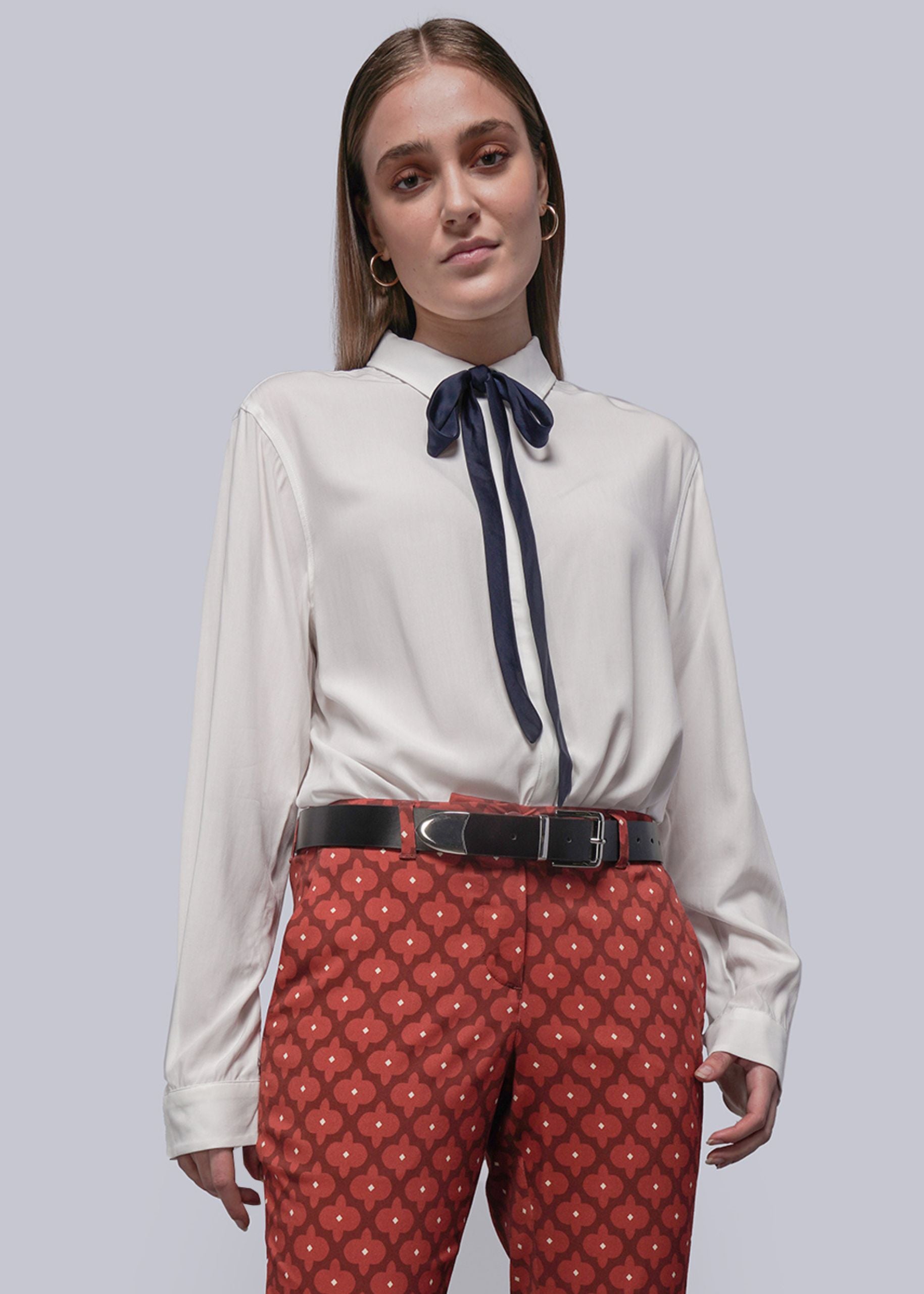 S=Woman wearing a white blouse with a navy bow and red patterned pants on a gray background
