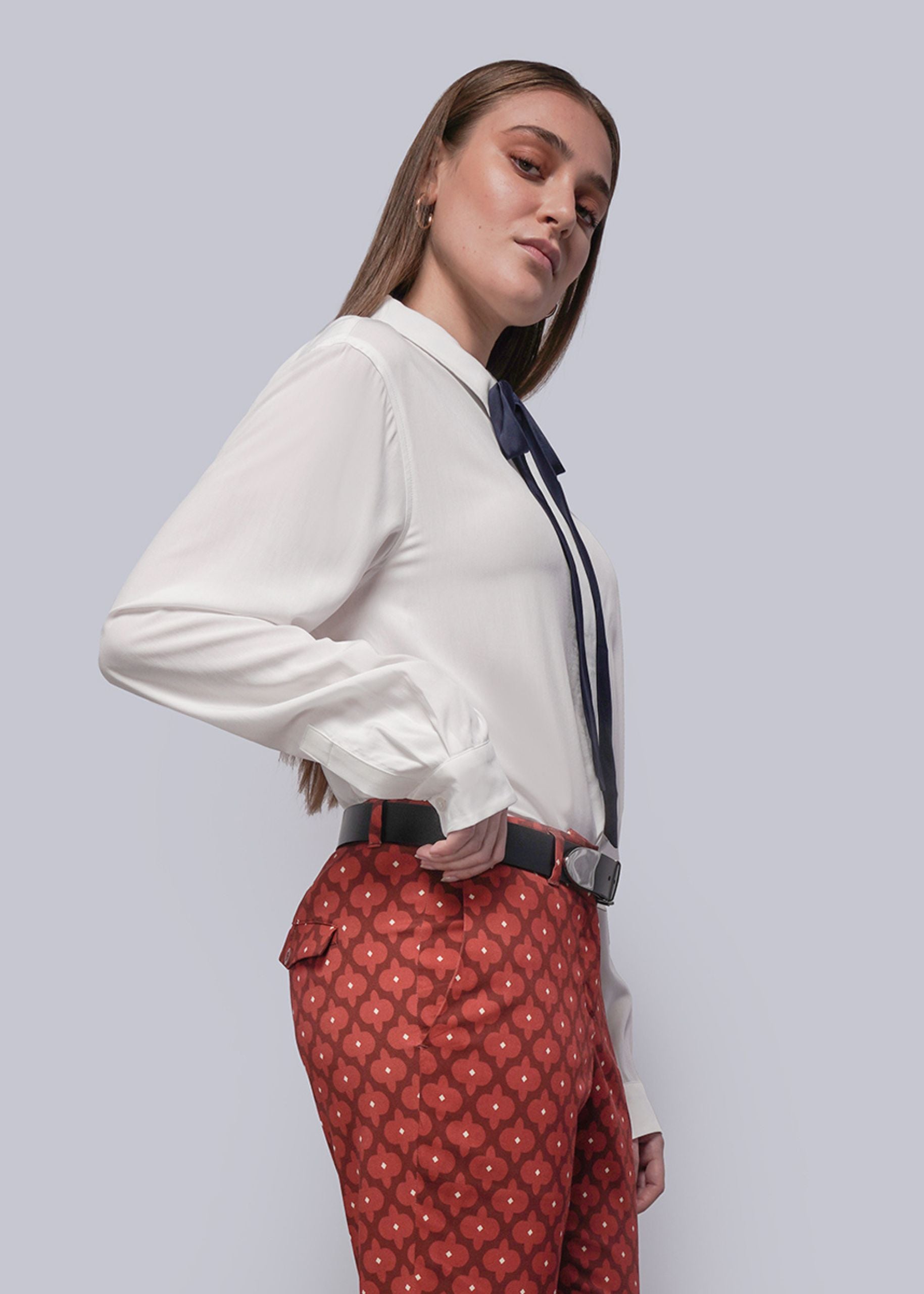 Person wearing a white blouse and red patterned pants against a light gray background