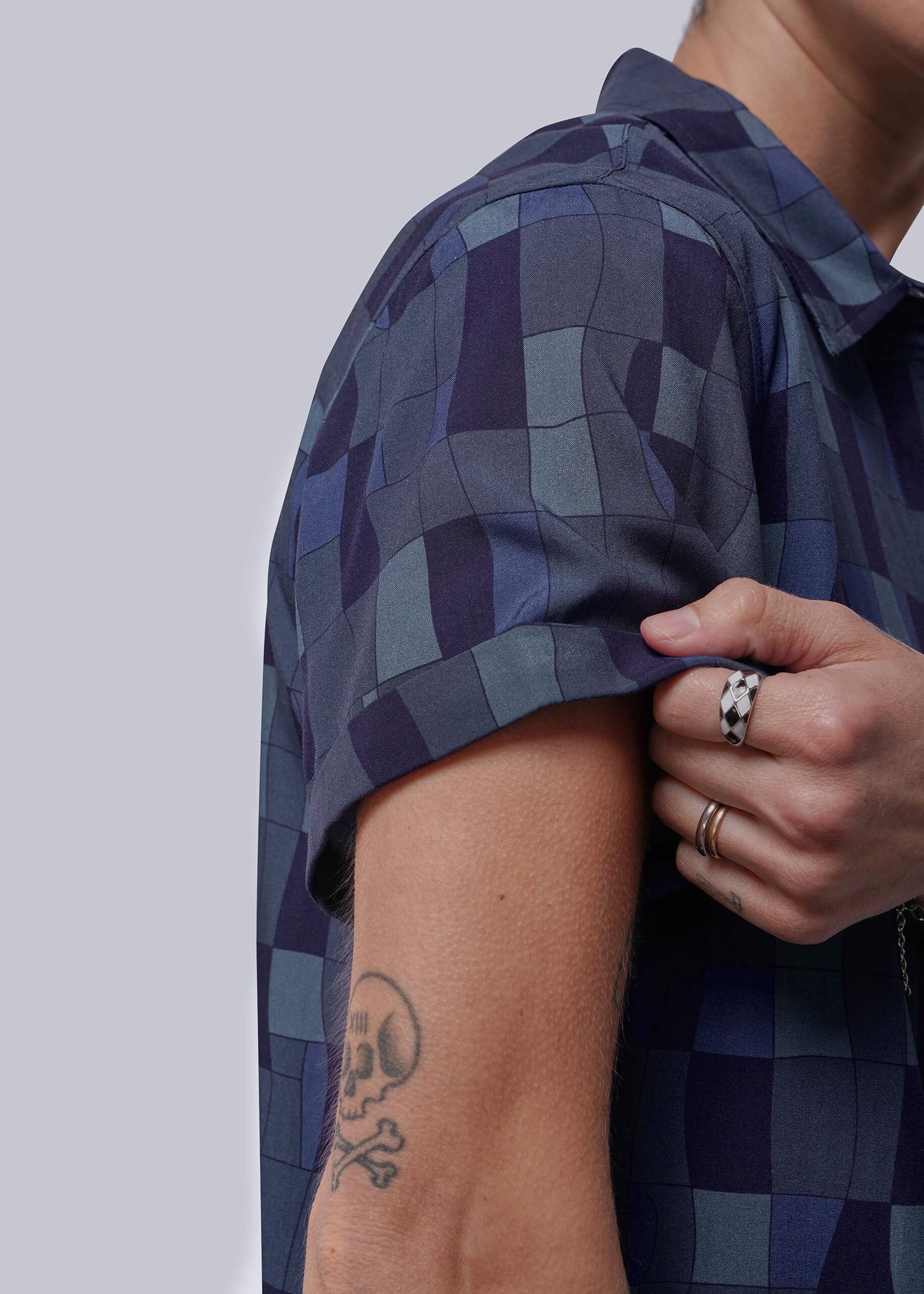 S=Close up of person wearing a blue checkered shirt showing the sleeve cuff with a plain background