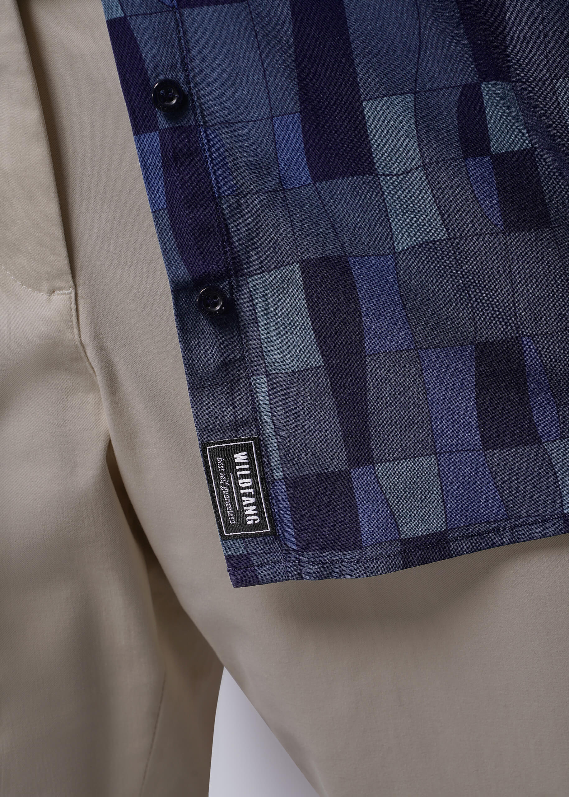 1X=Close-up of a blue checkered shirt over beige pants, featuring a Wildfang label.