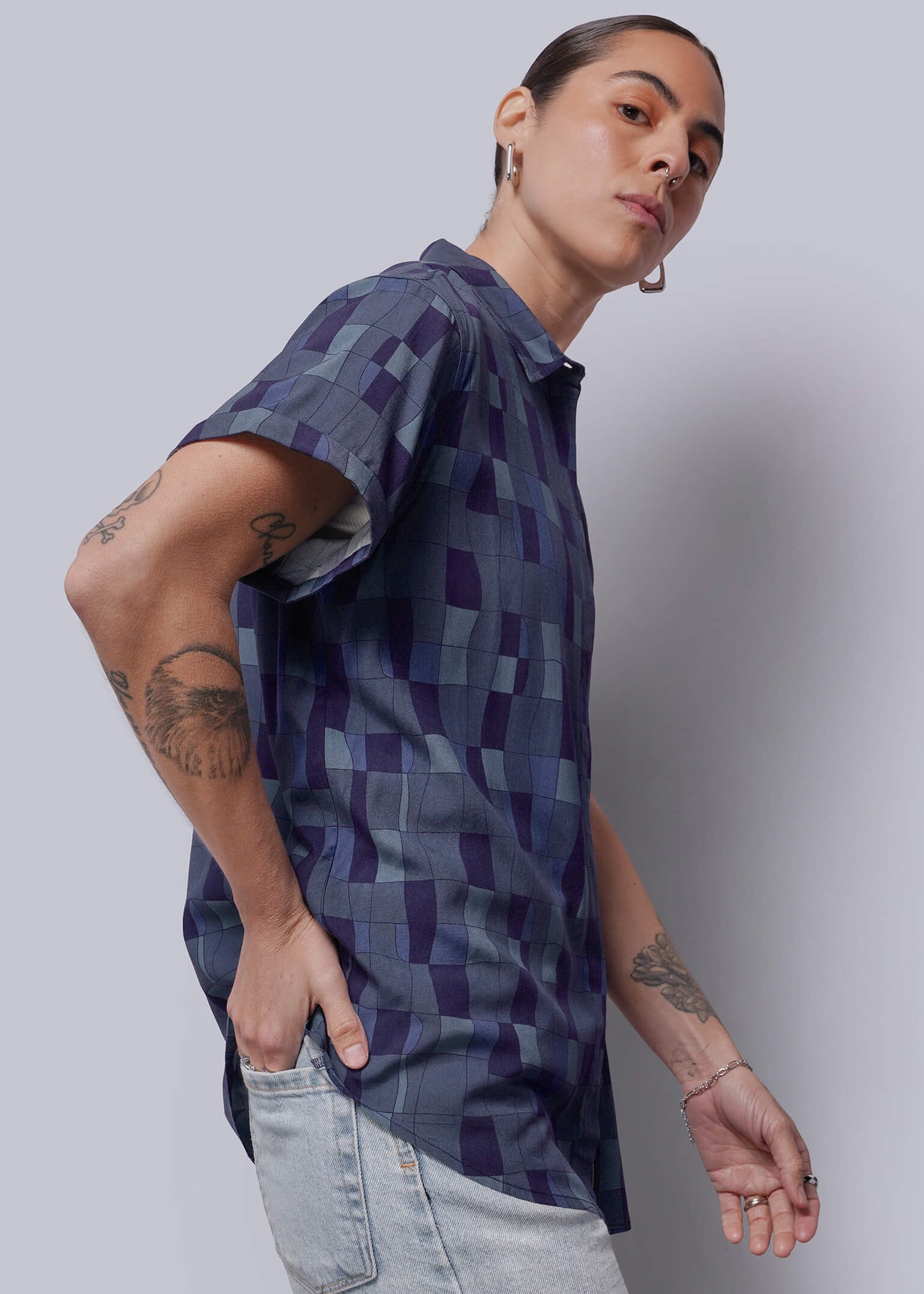 S=Person wearing a patterned shirt and light jeans against a plain background