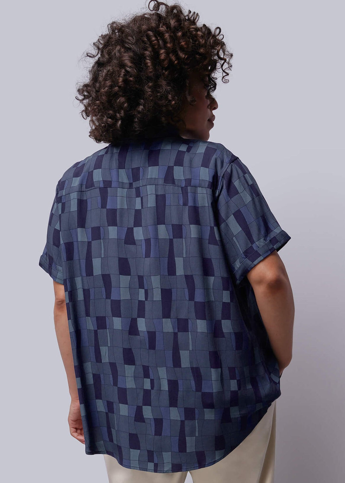 1X=Person wearing a blue patterned shirt and beige pants against a white background