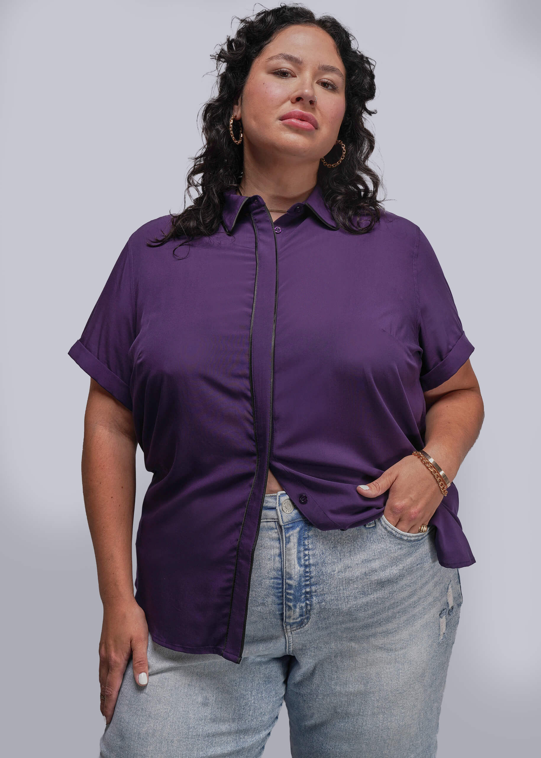 1X=Woman wearing a purple shirt and light blue jeans against a gray background