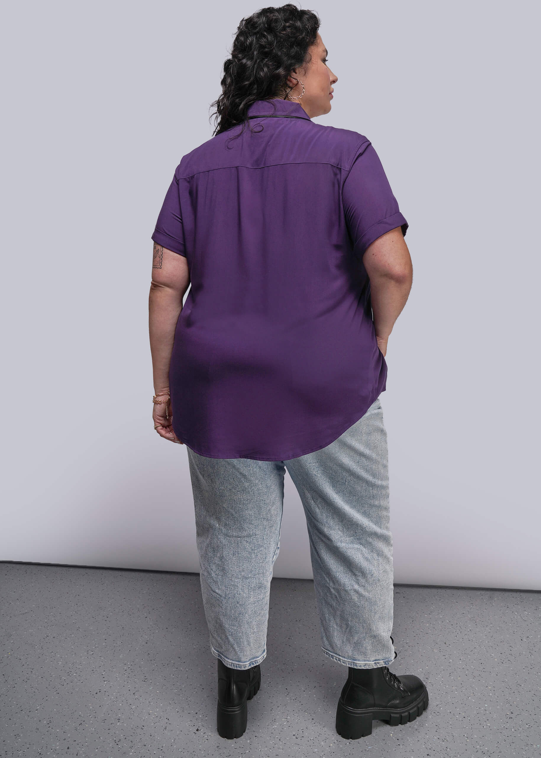 1X=Person wearing a purple shirt and gray pants against a white background