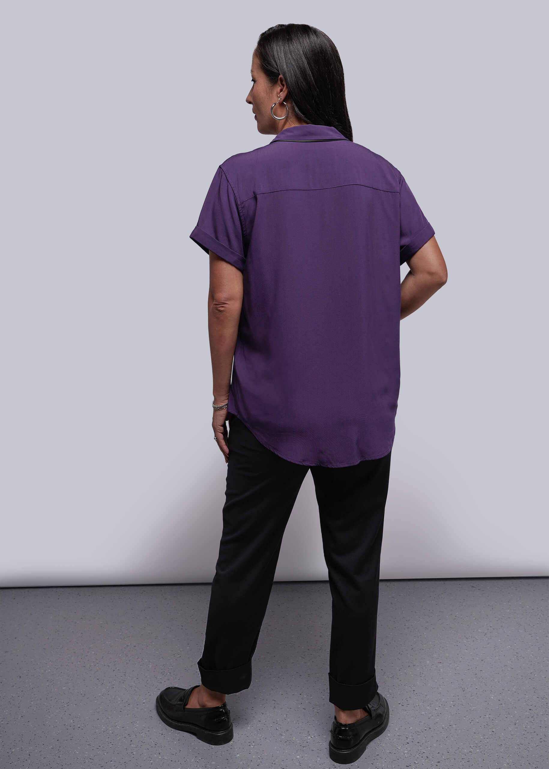S=Person wearing a purple shirt and black pants against a plain background