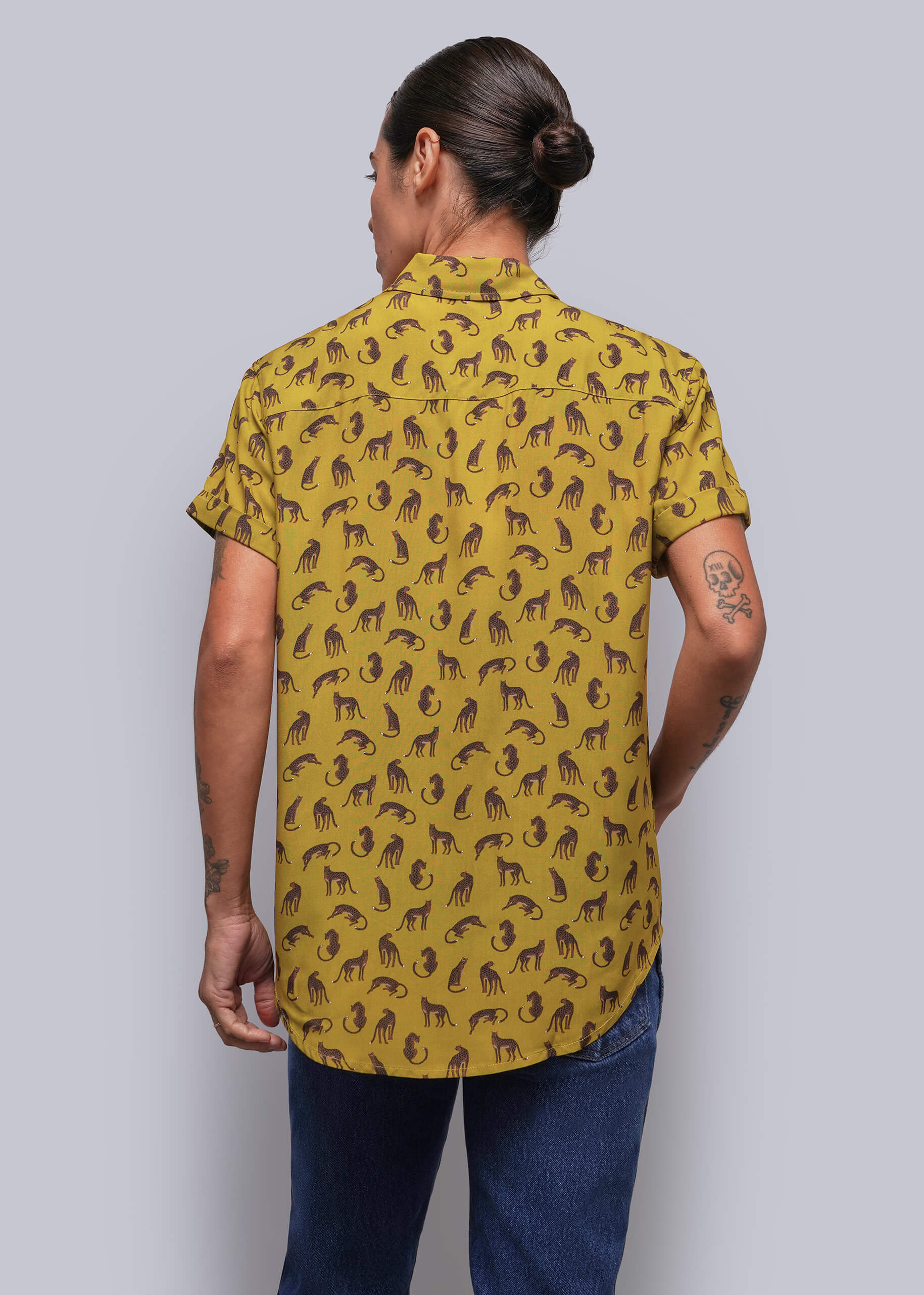 S=A person viewed from the back wearing a mustard yellow short-sleeve button-up shirt with a brown feline pattern, paired with blue jeans, against a solid gray background.