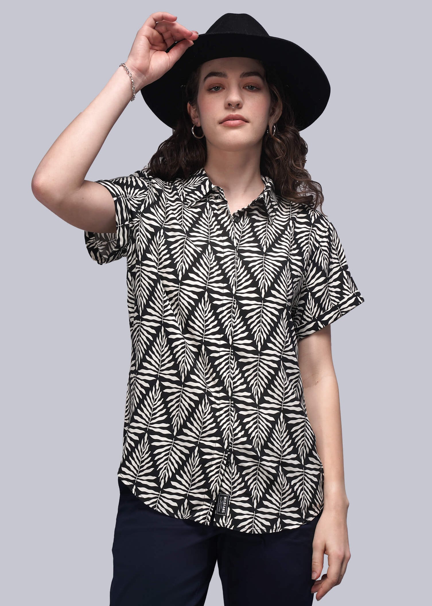 S=Woman wearing a black and white patterned blouse with a black hat on a gray background