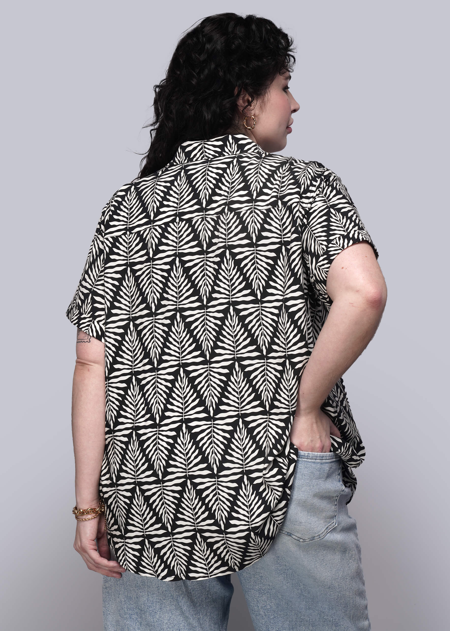 1X=Person wearing a black and white patterned shirt with short sleeves on a plain background