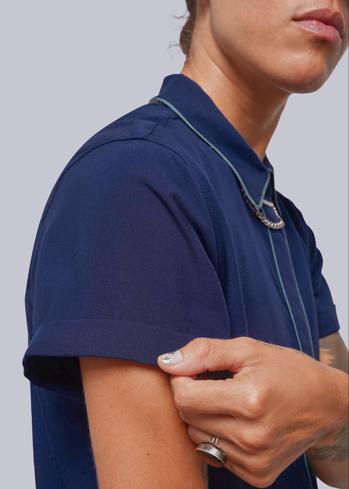 S=Close-up of a person wearing a navy blue short-sleeve polo shirt, showing the side profile and arm, against a light gray studio background.
