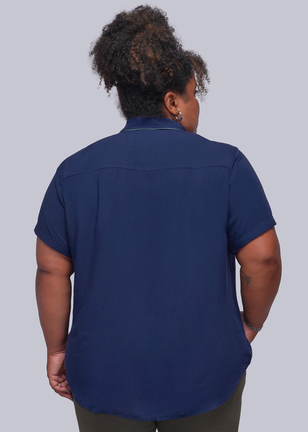 1X-A person shown from the back wearing a navy blue short-sleeve button-up shirt and olive green pants, photographed against a solid light gray studio background.
