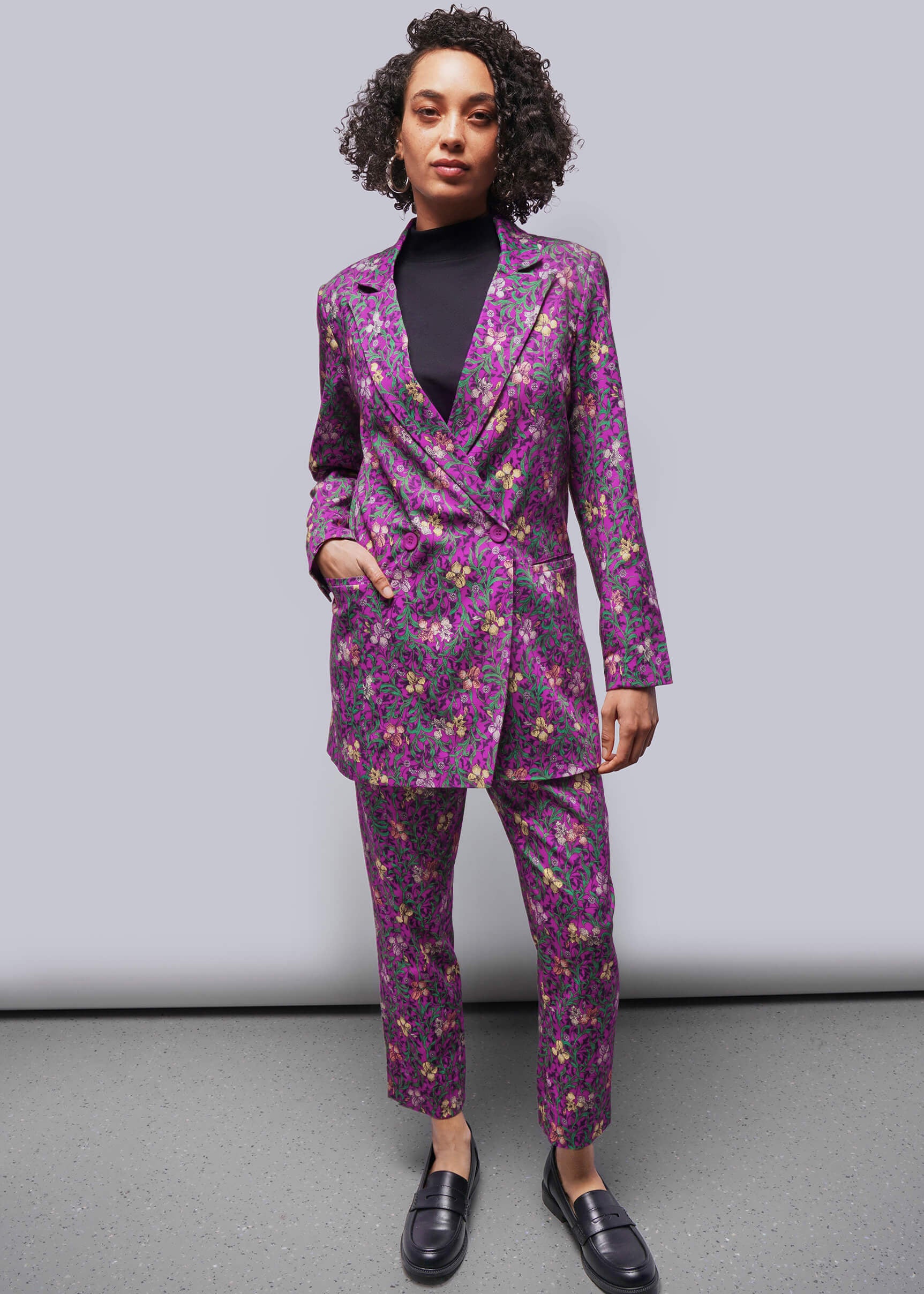 S=Person wearing a purple floral suit against a gray background