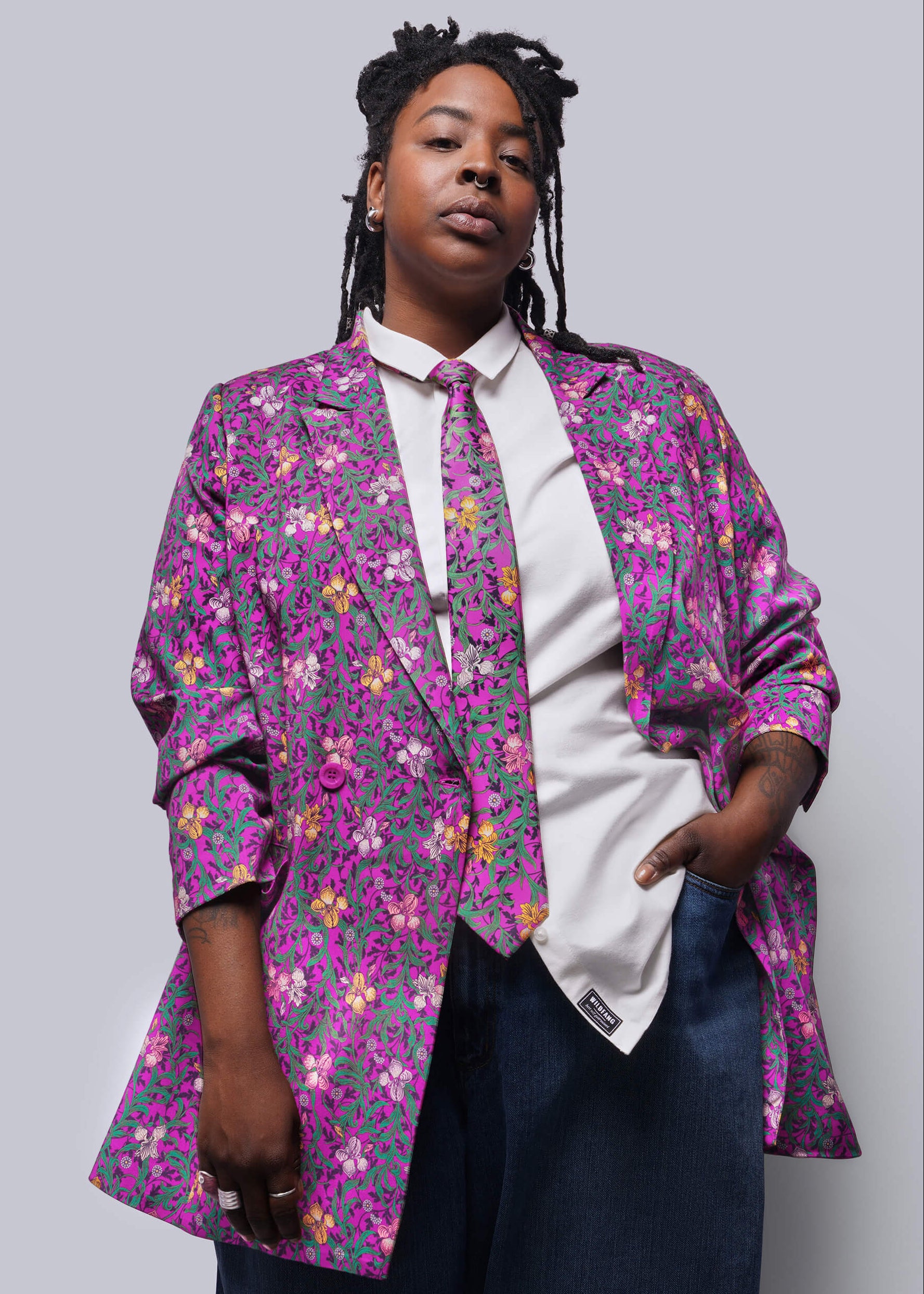 1X=Person wearing a colorful floral blazer over a white shirt on a plain background