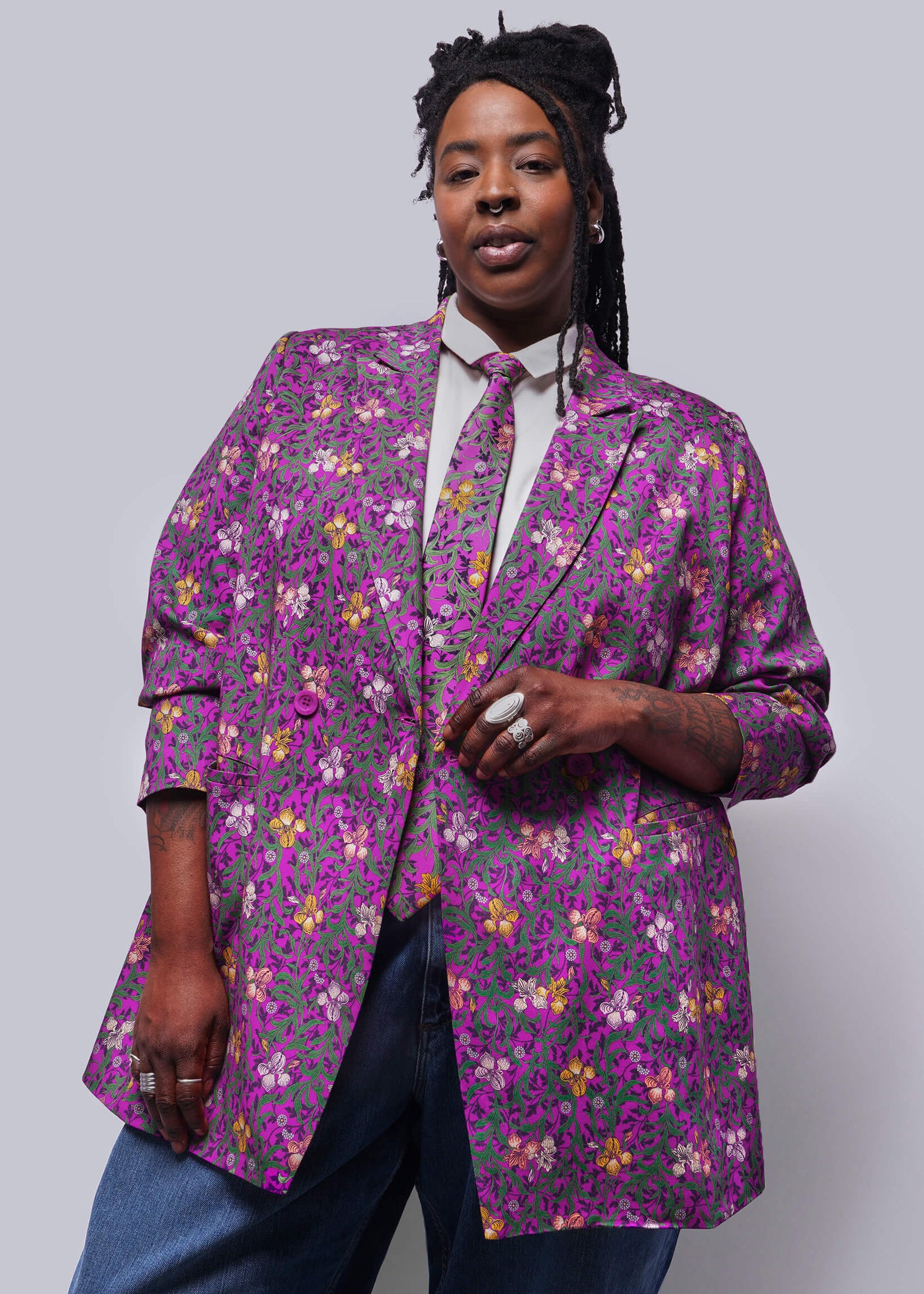 1X=Person wearing a purple floral blazer against a plain background
