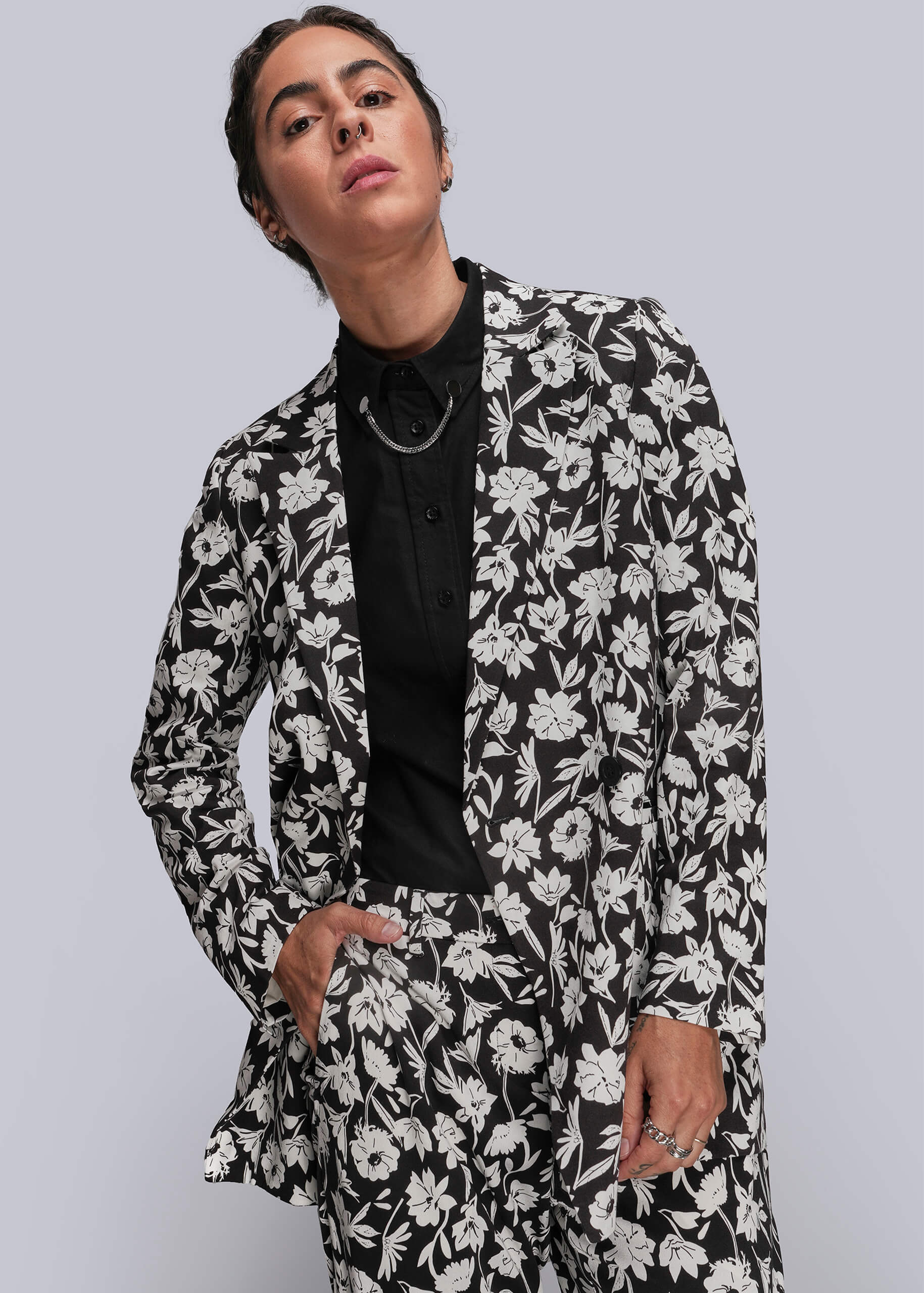 S=Person wearing a black and white floral suit against a gray background
