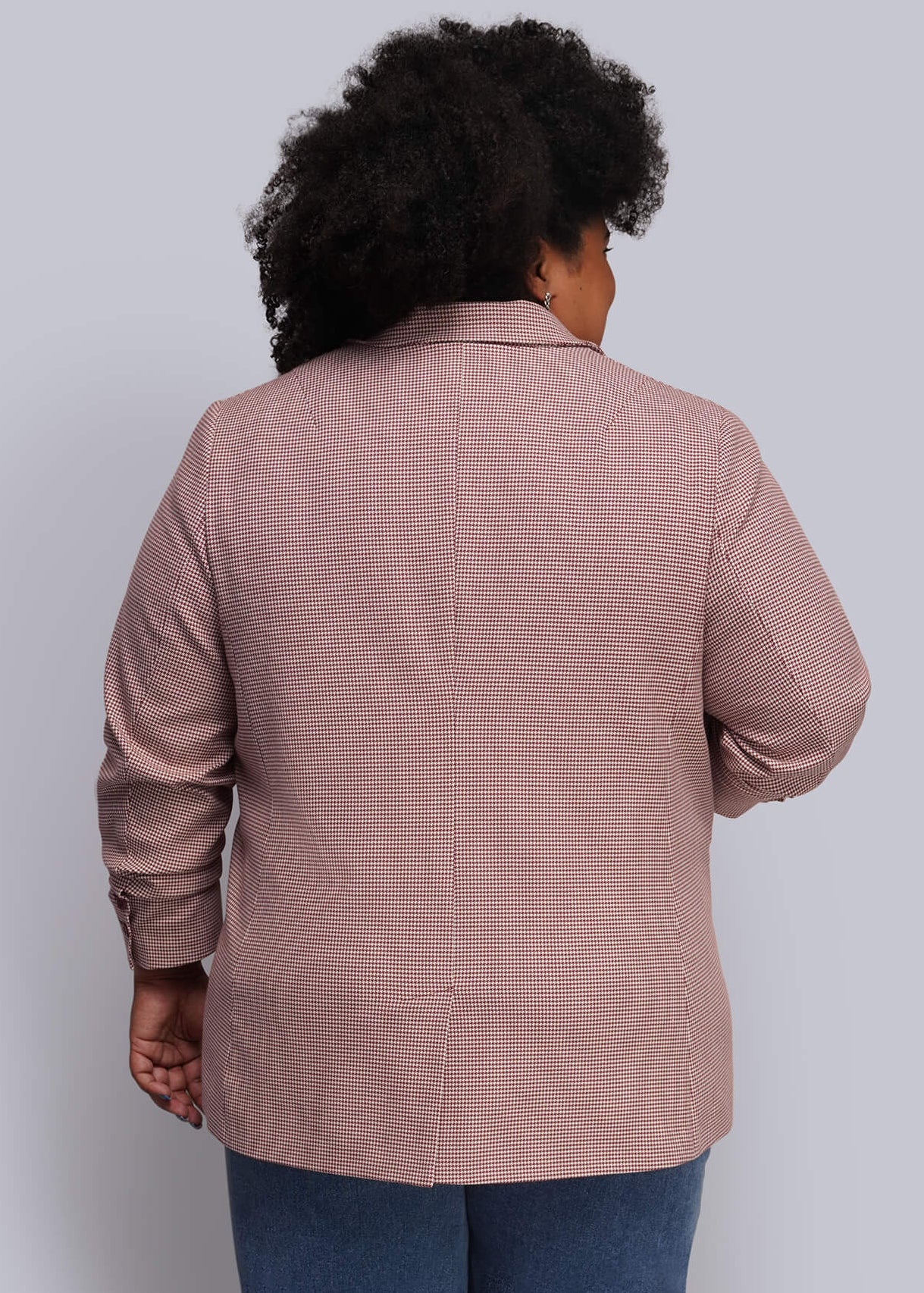 1X=A person shown from the back wearing a dusty red blazer and wide-leg blue jeans, standing against a plain light gray wall.