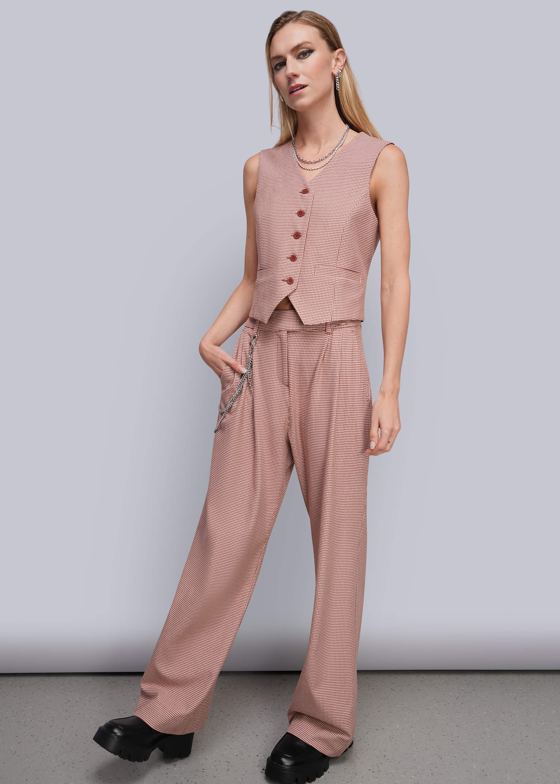 A woman modeling a dusty red sleeveless vest and matching wide-leg trousers, styled with black platform shoes against a plain light gray studio background.