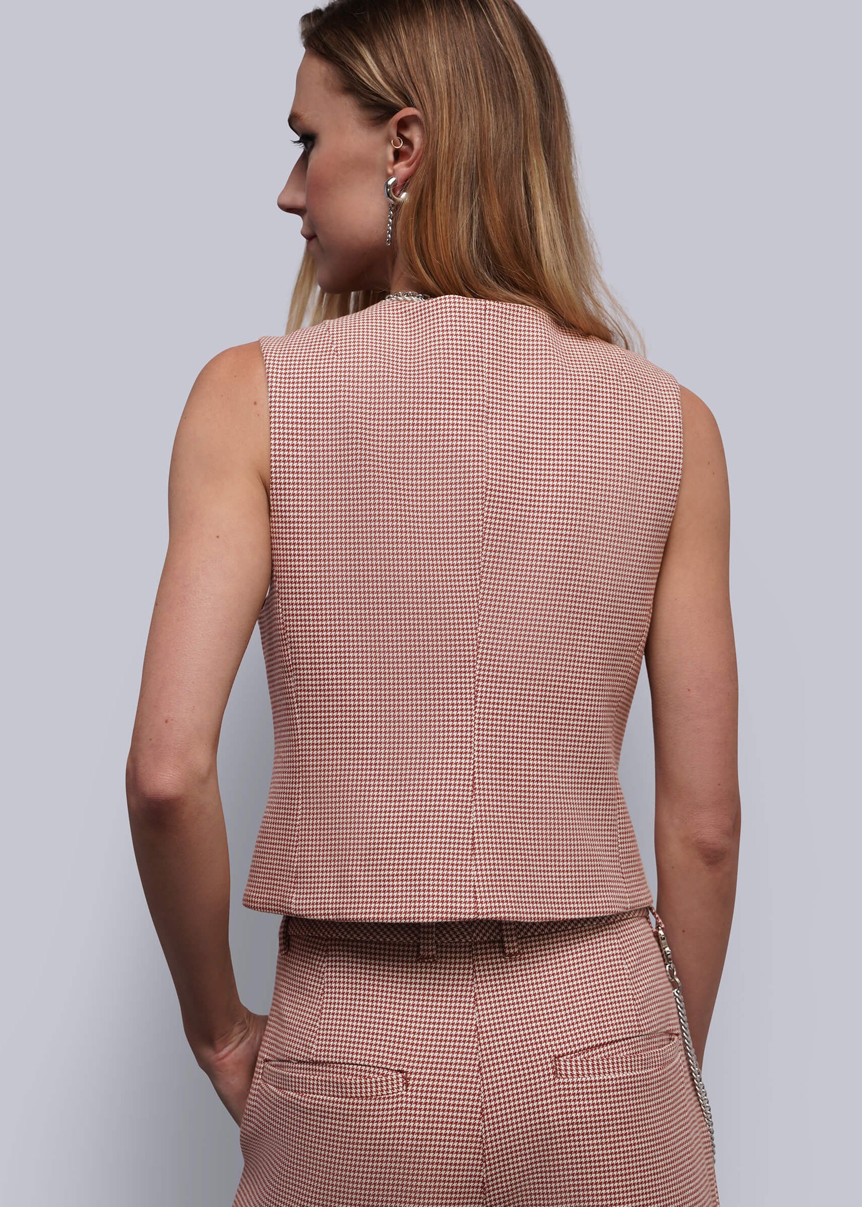 S=A woman shown from the back wearing a sleeveless vest and matching trousers in a houndstooth pattern. The color is a dusty red and beige.