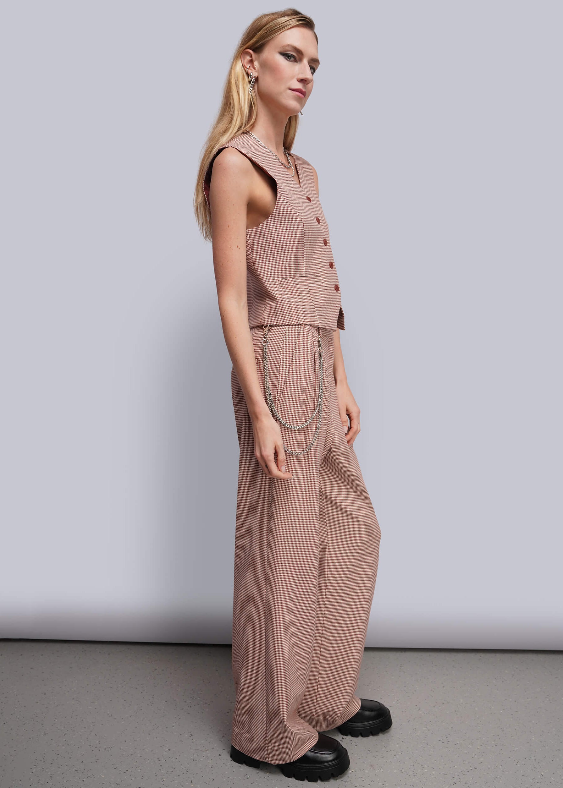 S=A woman modeling a sleeveless dusty red suit with wide-leg pants, paired with black platform shoes against a light gray studio background.