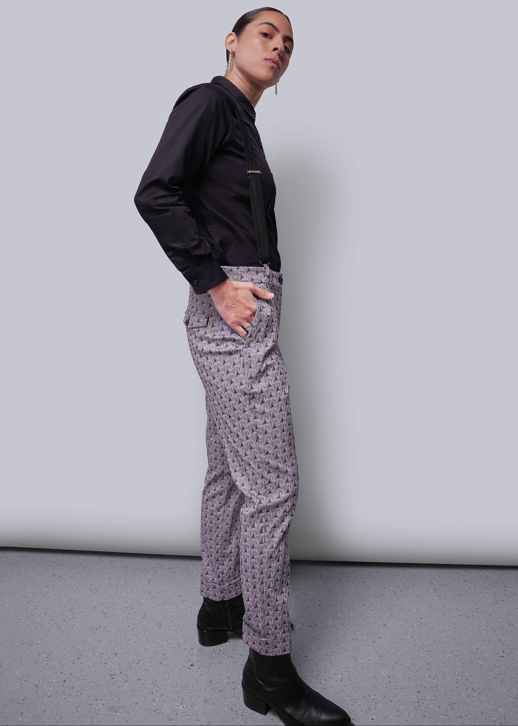Person wearing a black shirt and patterned pants against a plain background
