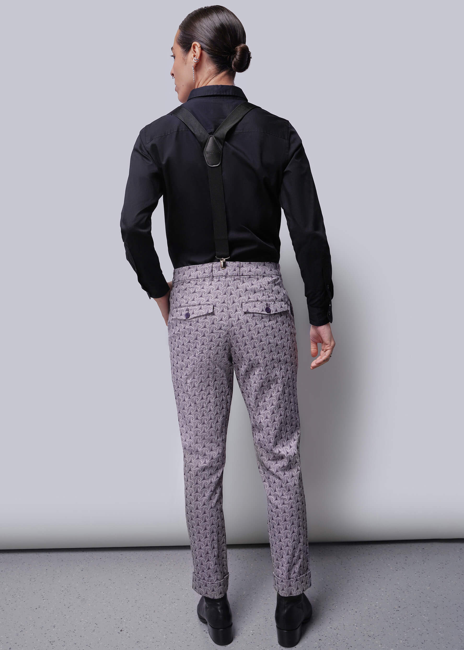 S=Person wearing a black shirt and patterned pants against a plain background