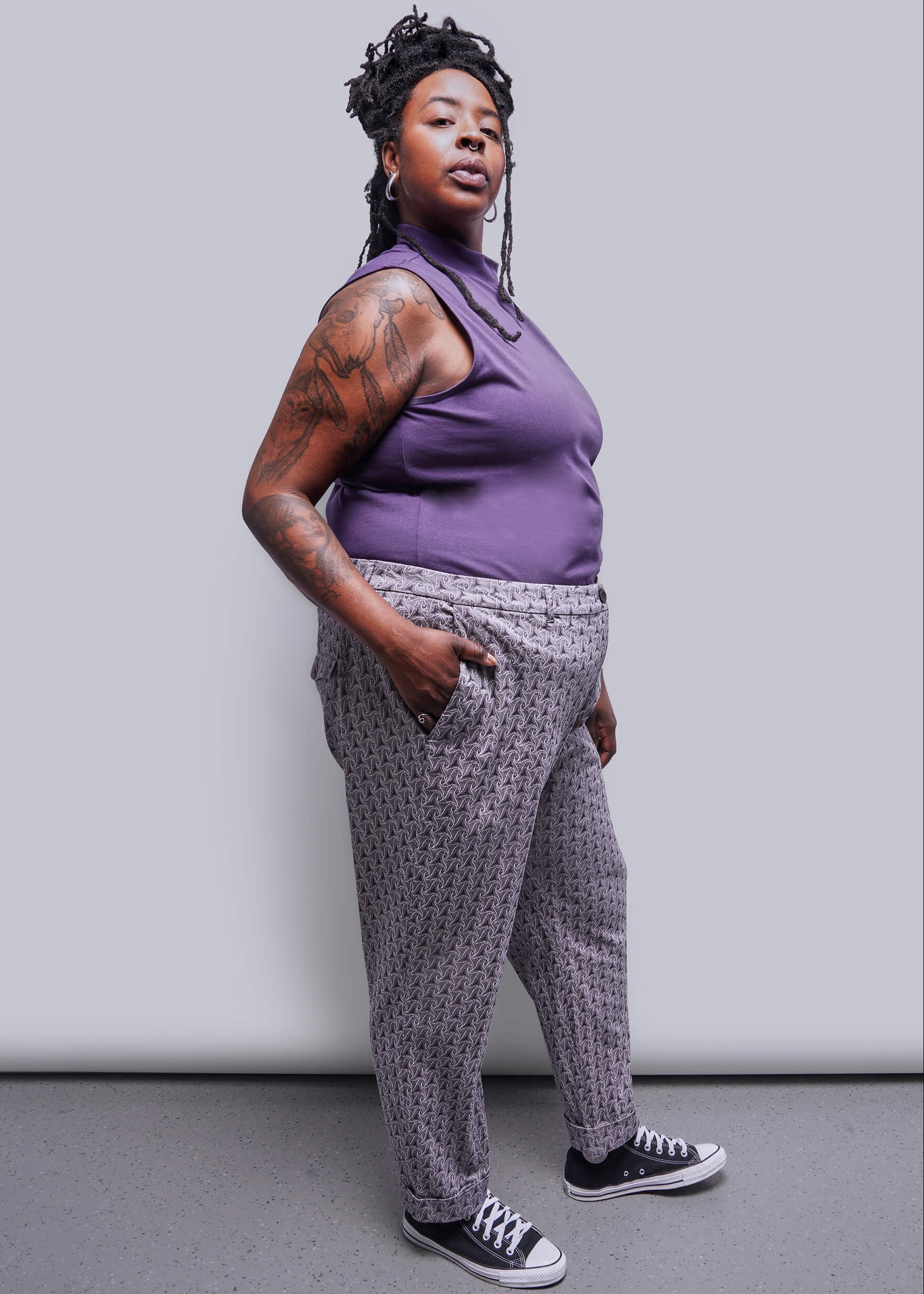 1X=Person wearing a purple sleeveless top and patterned pants against a plain background