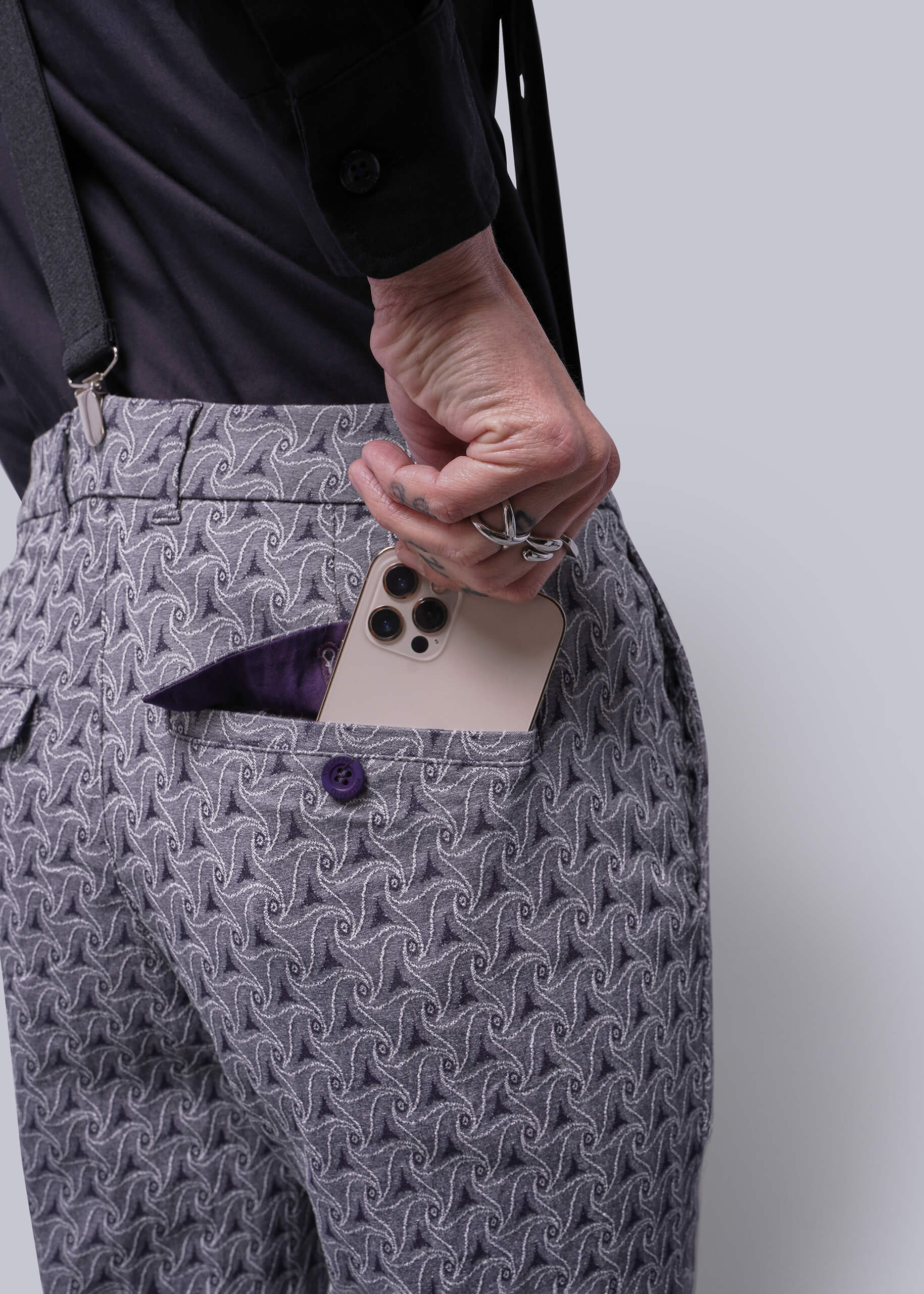 S=Person wearing gray patterned pants with a white object in a pocket against a plain background