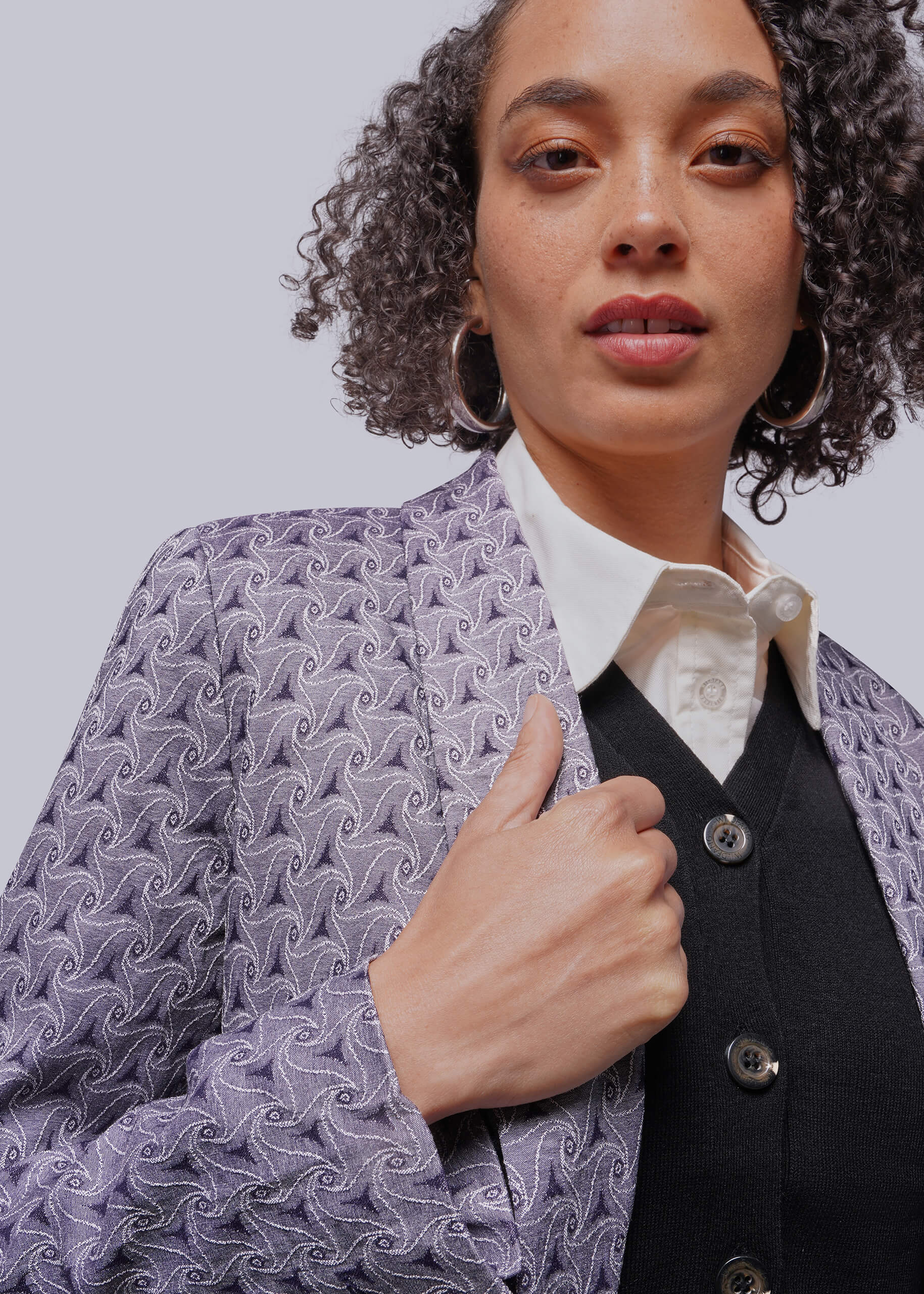 Person wearing a patterned jacket over a white shirt and black vest on a light gray background