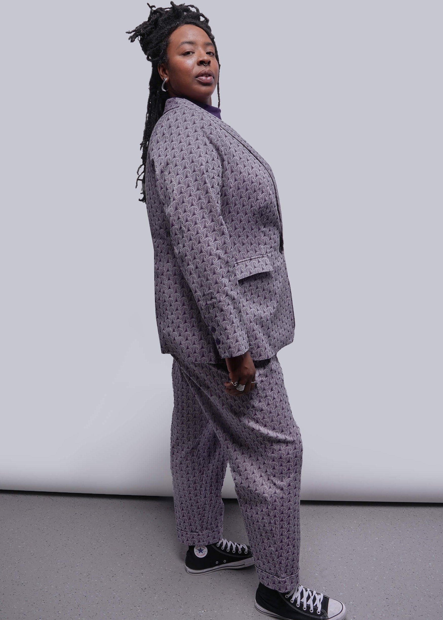 1X=Person wearing a patterned suit with black and white sneakers against a plain background
