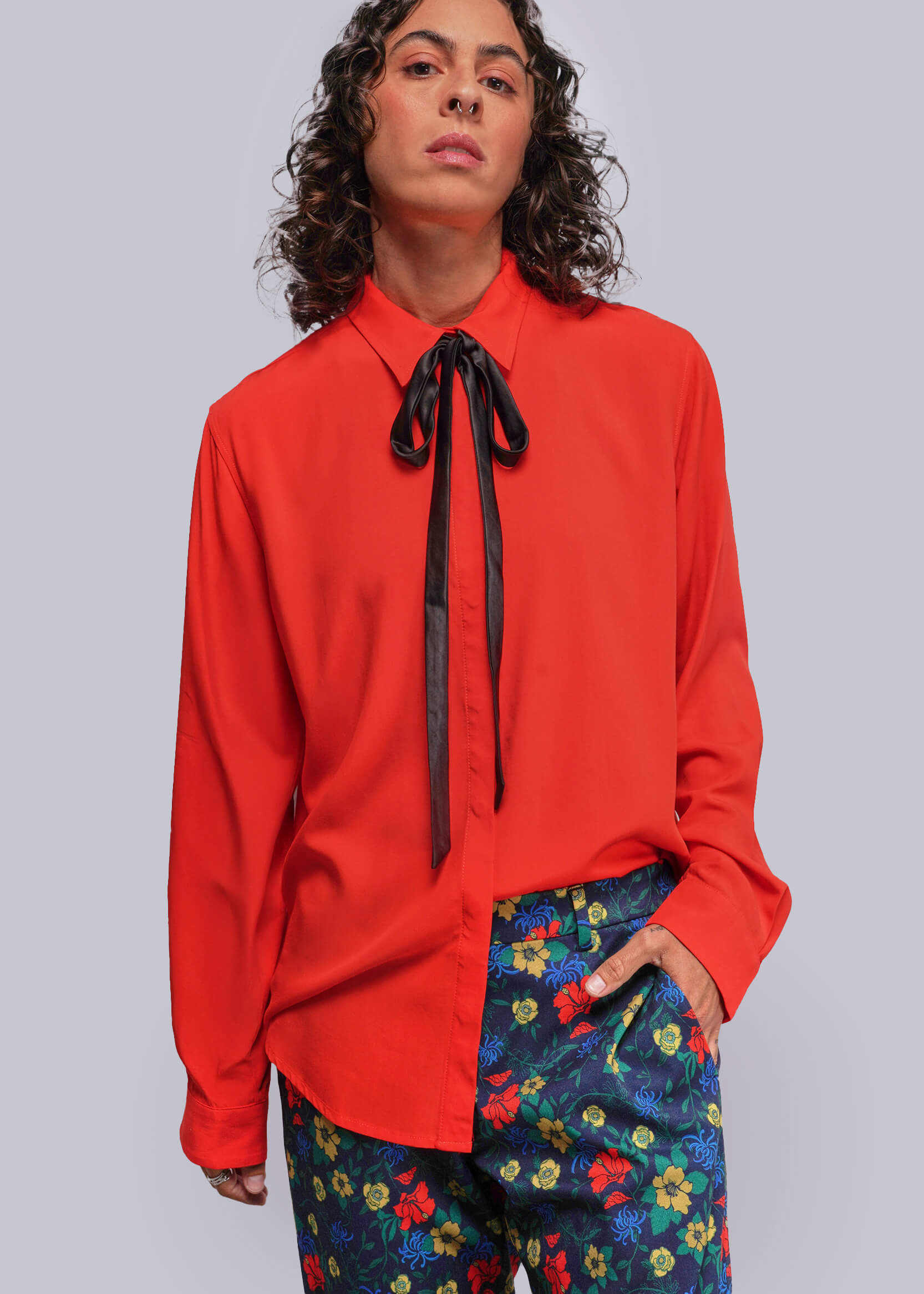 Person wearing a red blouse with a black ribbon and colorful pants on a gray background