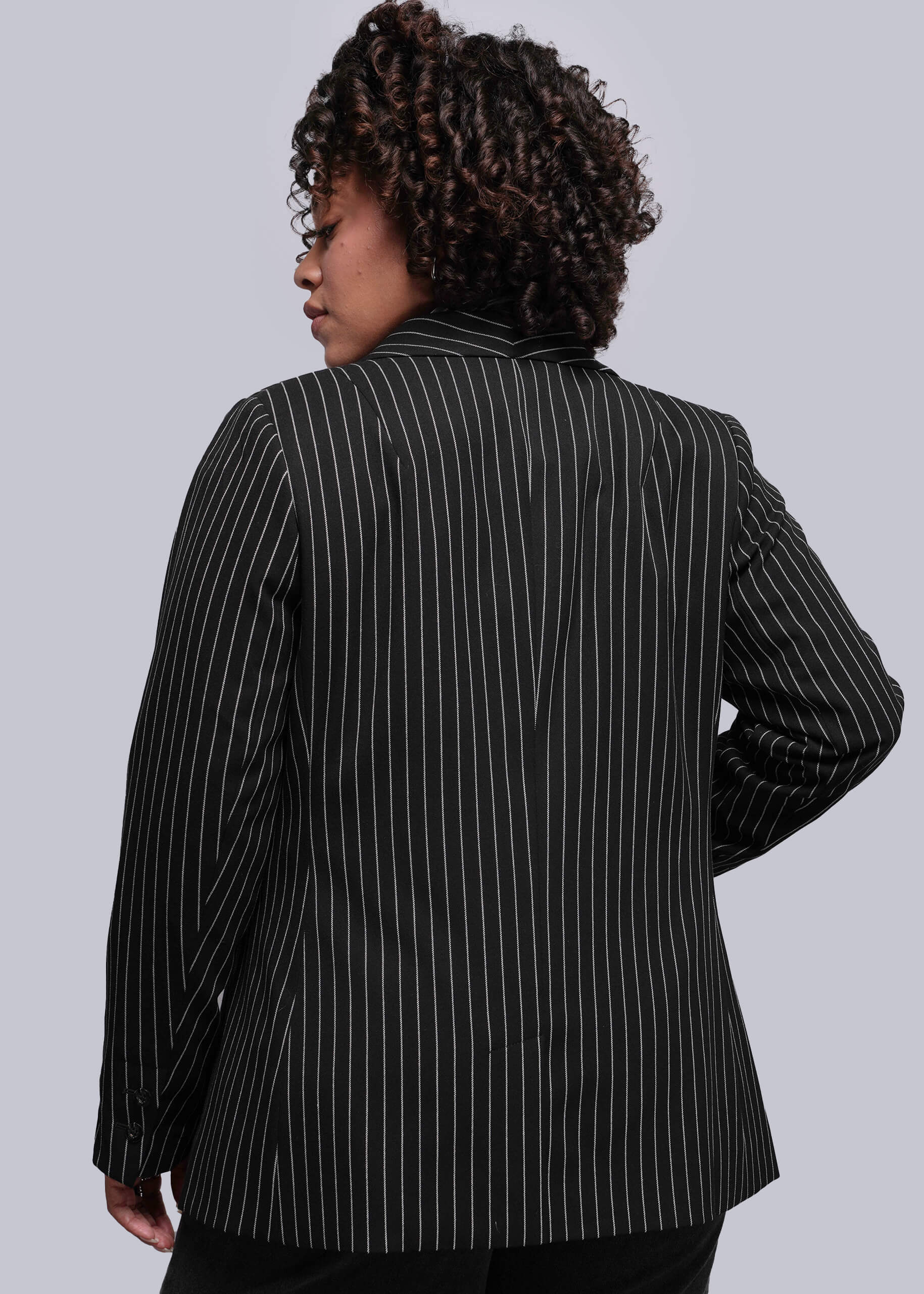 1X=Person wearing a black pinstripe blazer against a plain background