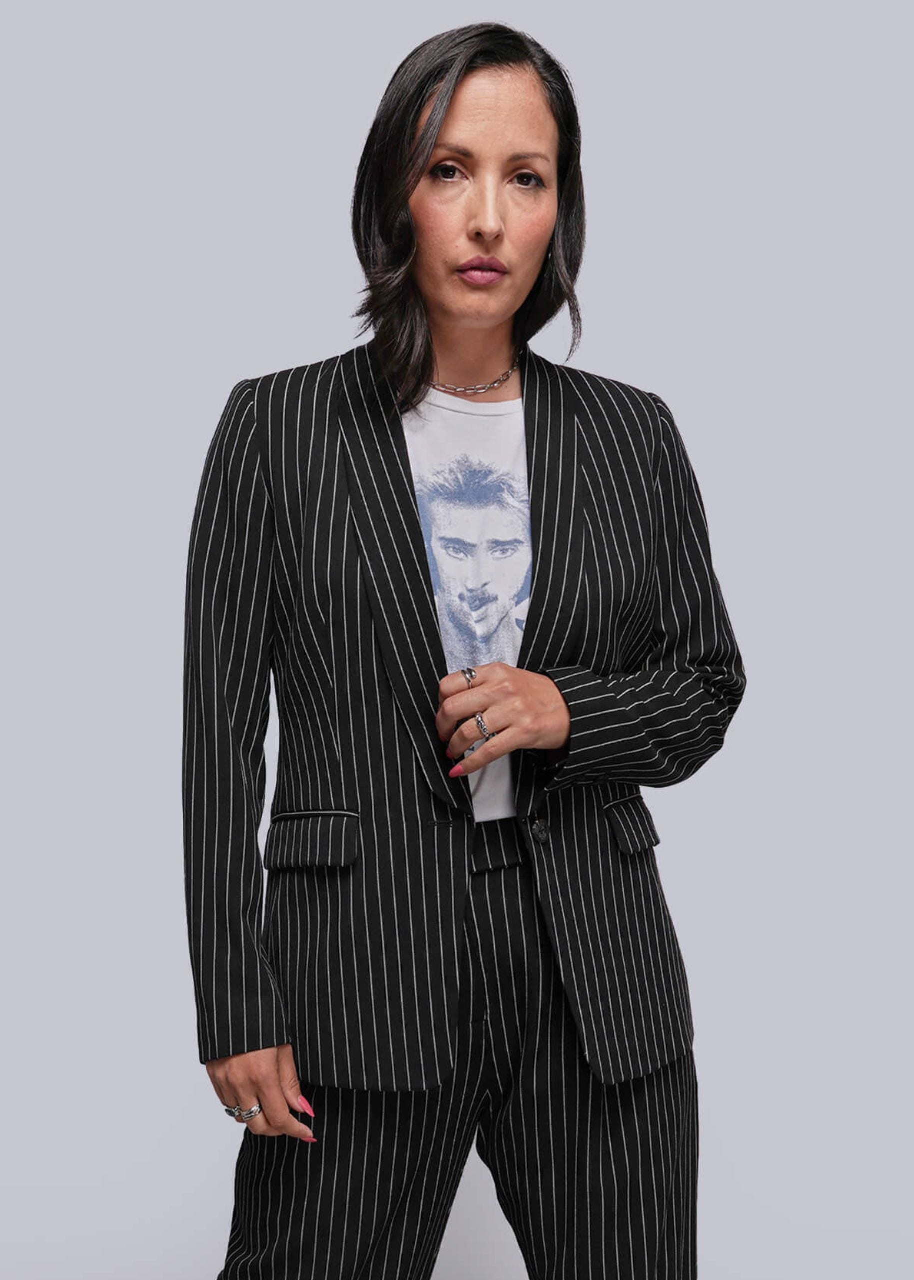 Woman wearing a black pinstripe suit over a light blue graphic t-shirt on a gray background