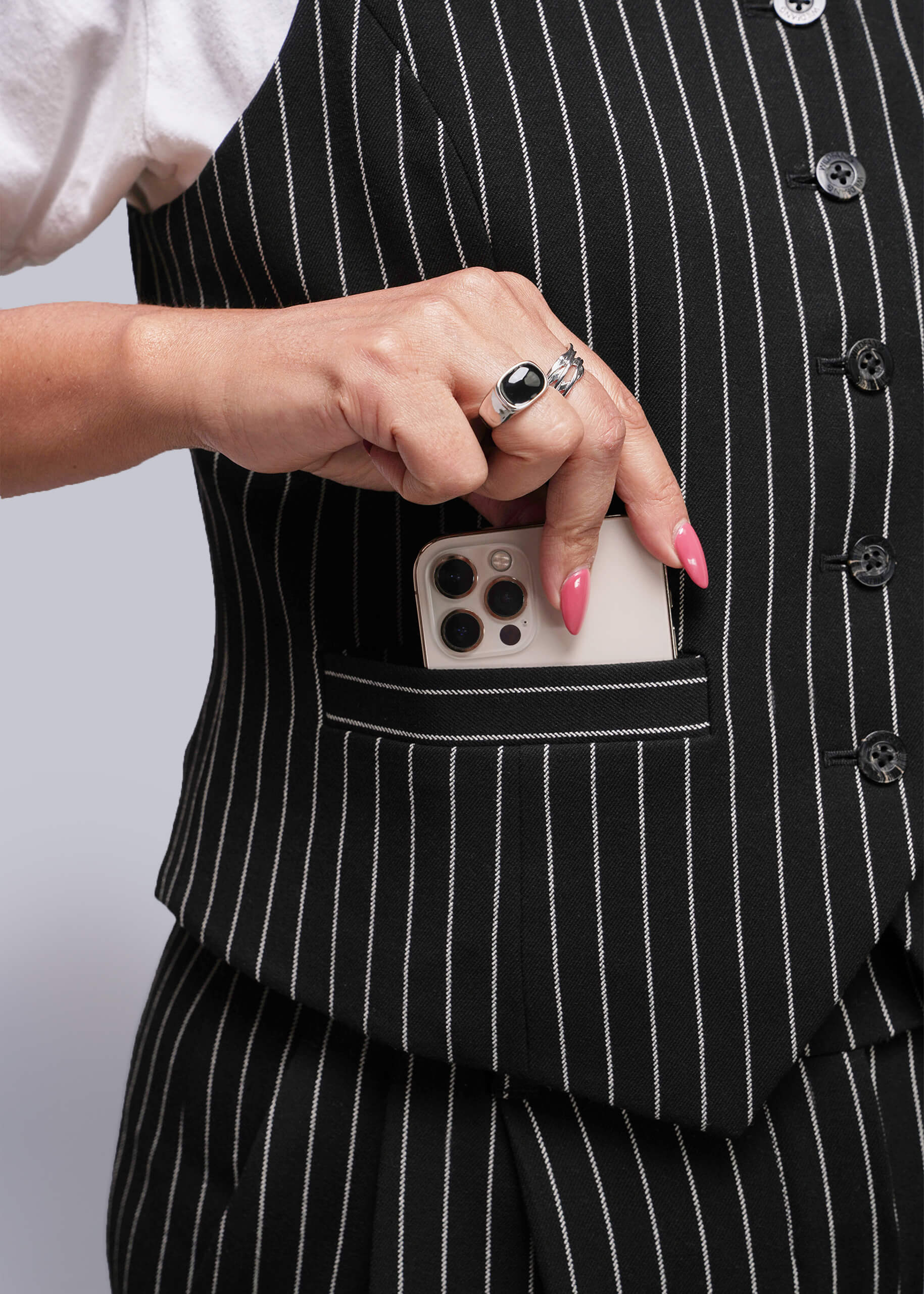 Person wearing a black pinstripe suit with a phone in the pocket against a neutral background