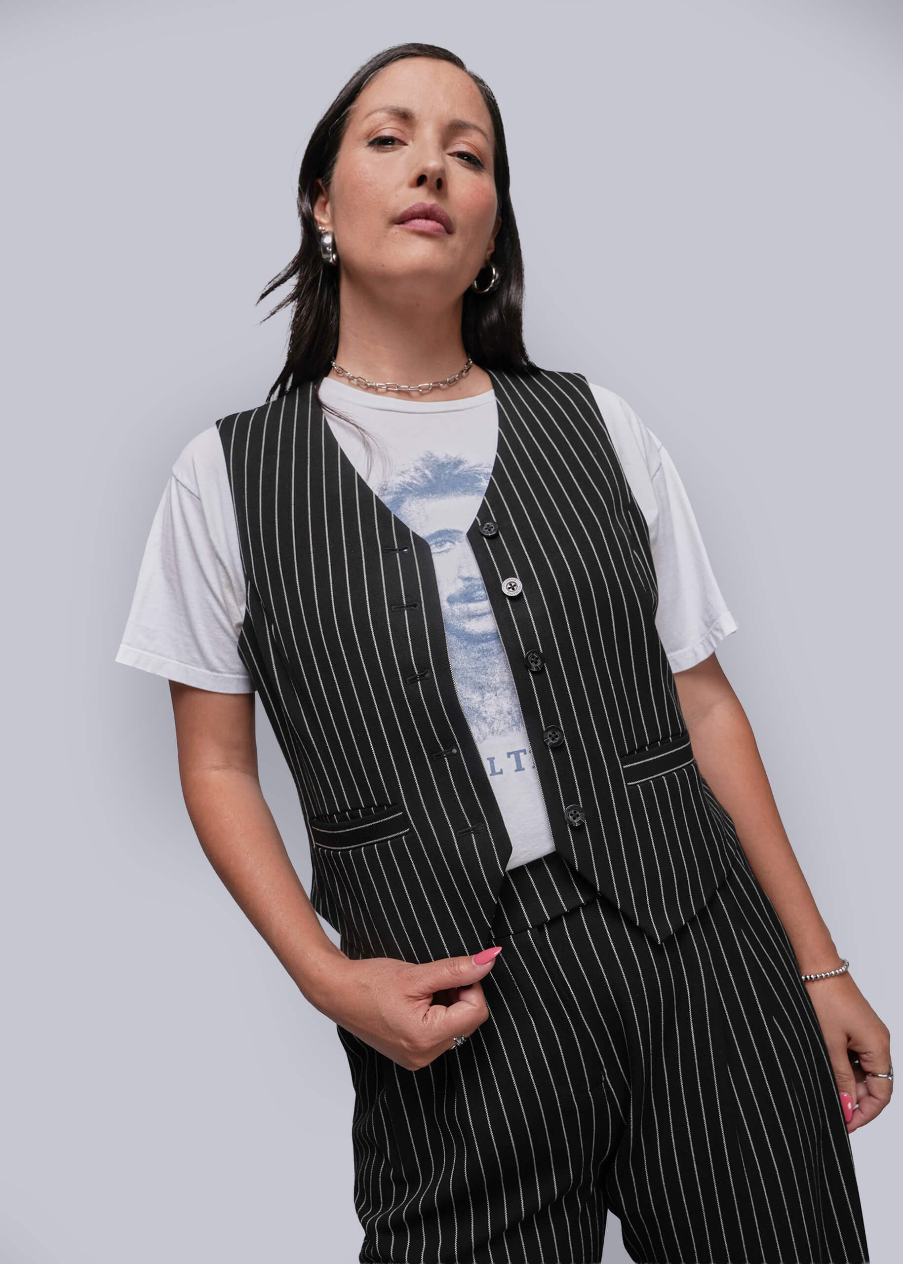Woman wearing a black pinstripe vest over a white t-shirt with a graphic design on a plain background