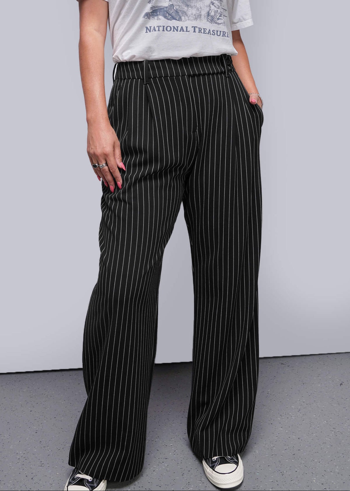 S=Person wearing a graphic t-shirt and pinstripe pants against a plain background