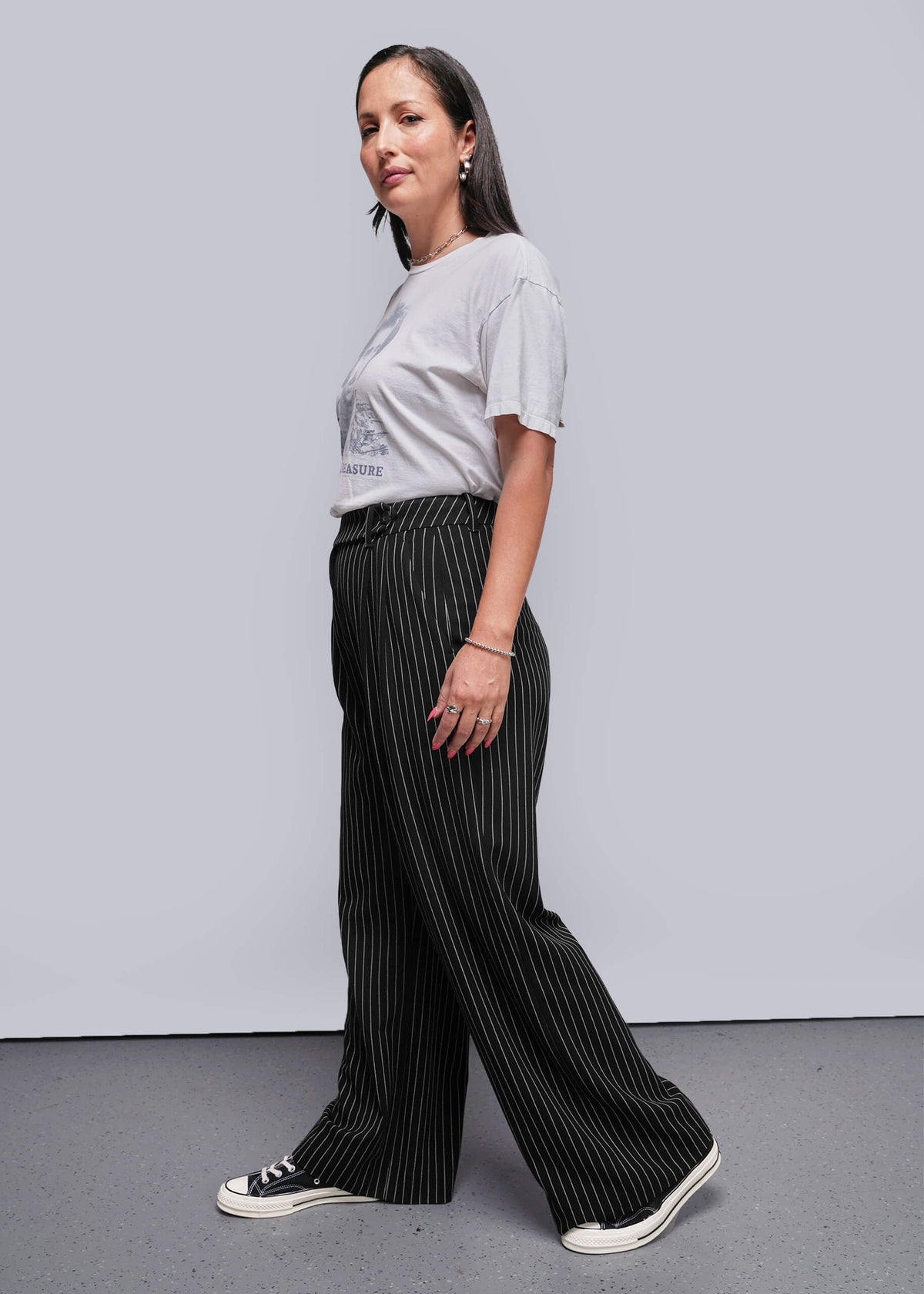 S=Woman wearing a white t-shirt and black pinstripe pants against a plain background