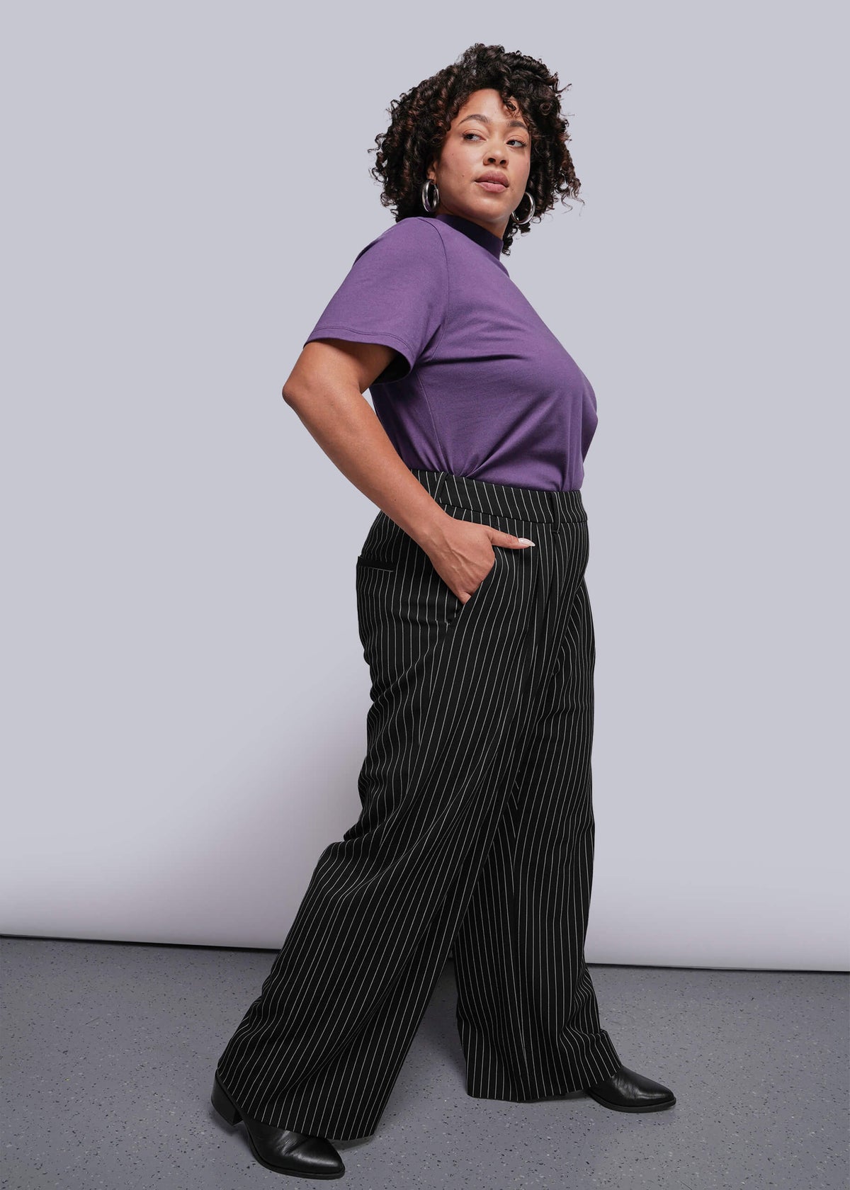 1X=Person wearing a purple top and black pinstripe pants against a plain background