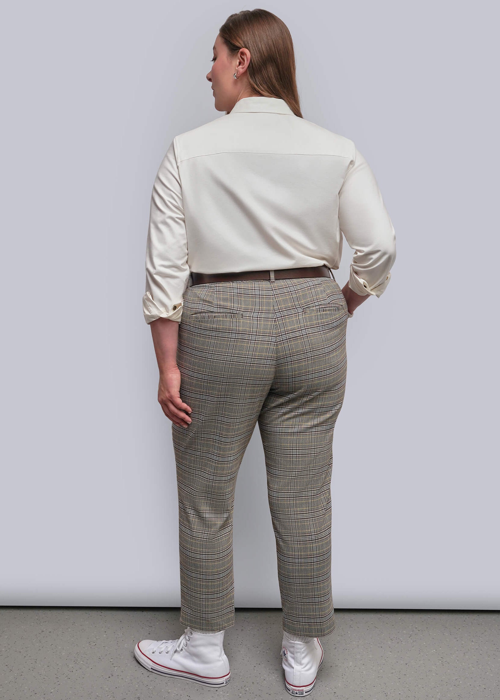 1X=A model shown from the back wearing a cream-colored long-sleeve shirt, beige and brown plaid trousers, and white sneakers against a plain light gray studio background.