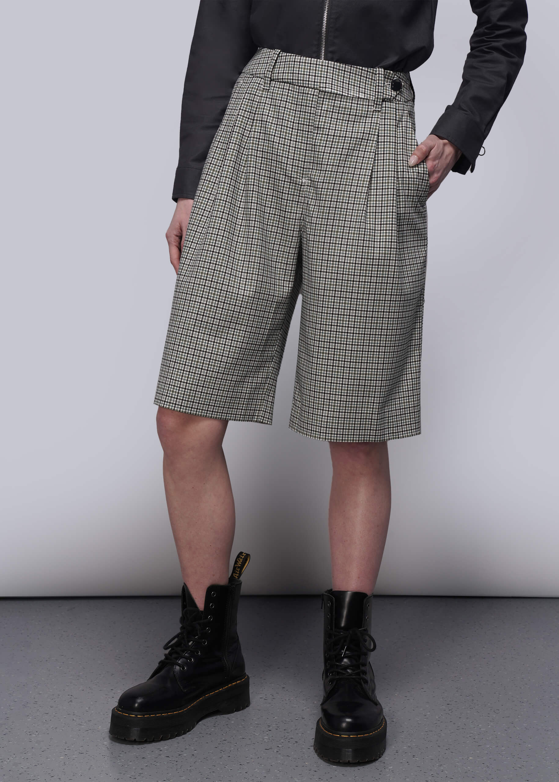 Person wearing checkered shorts and black boots on a plain background