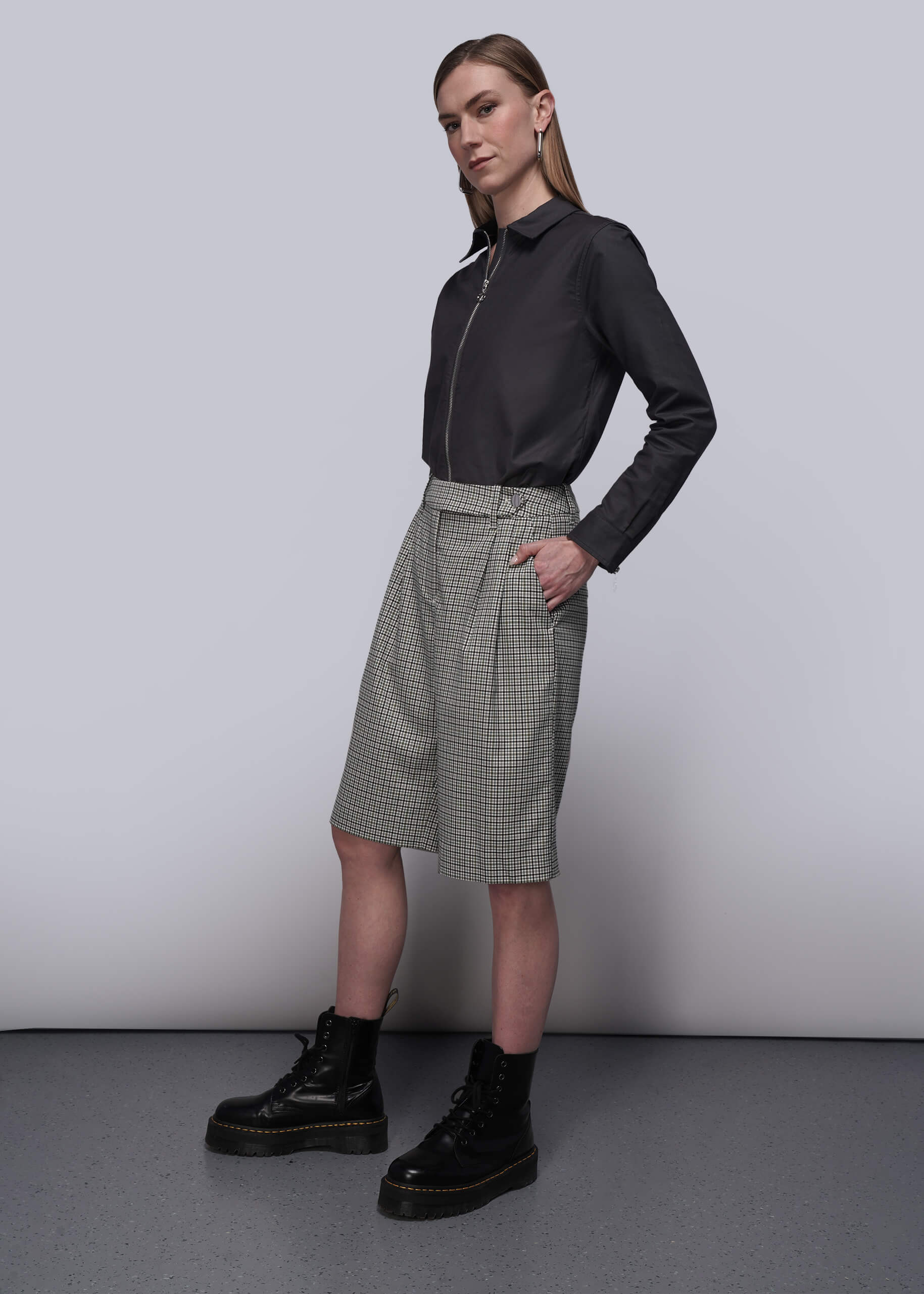 S=Person wearing a black shirt and checkered skirt with black shoes on a plain background
