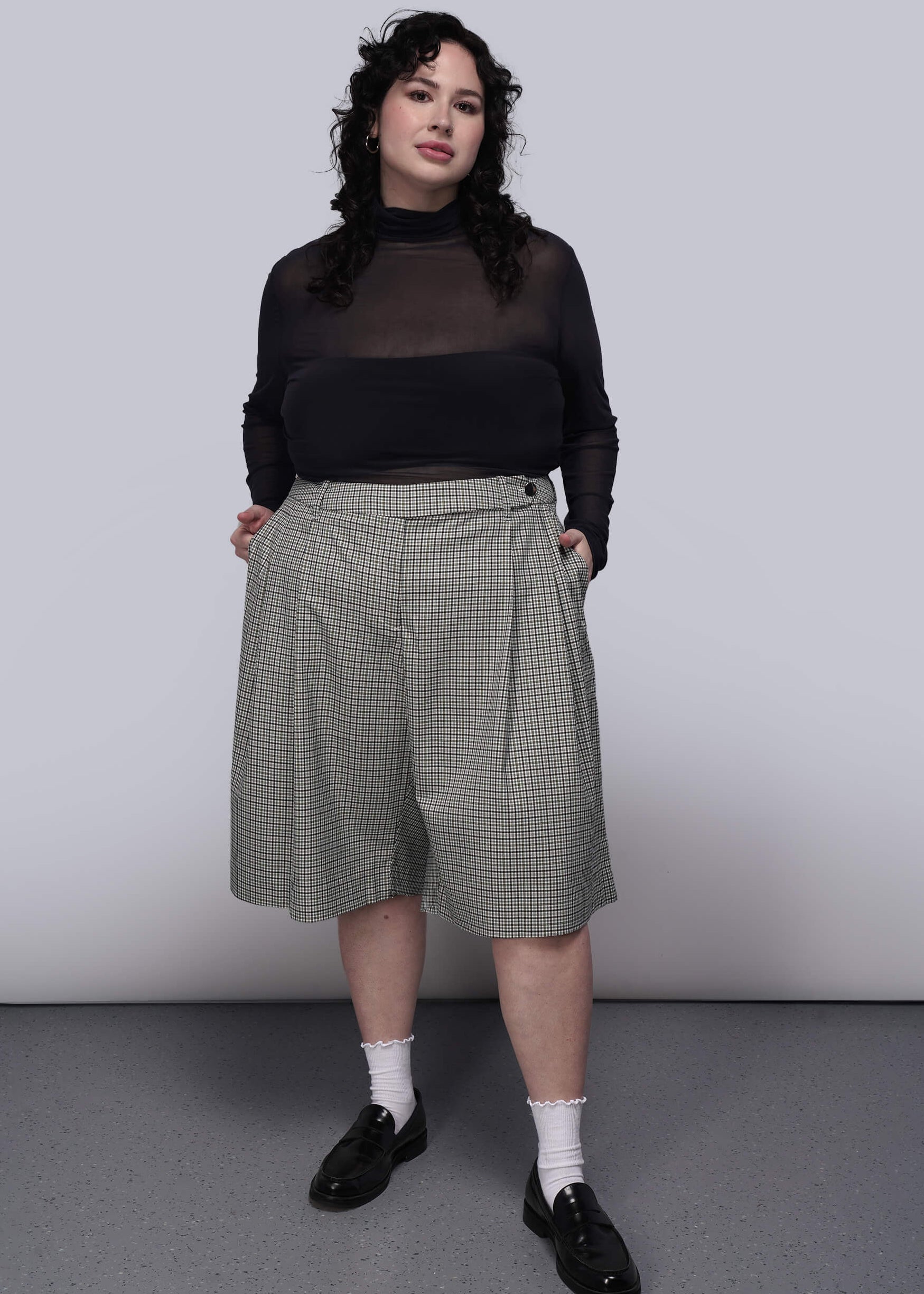 1X=Person wearing a black long sleeve top and plaid shorts against a plain background