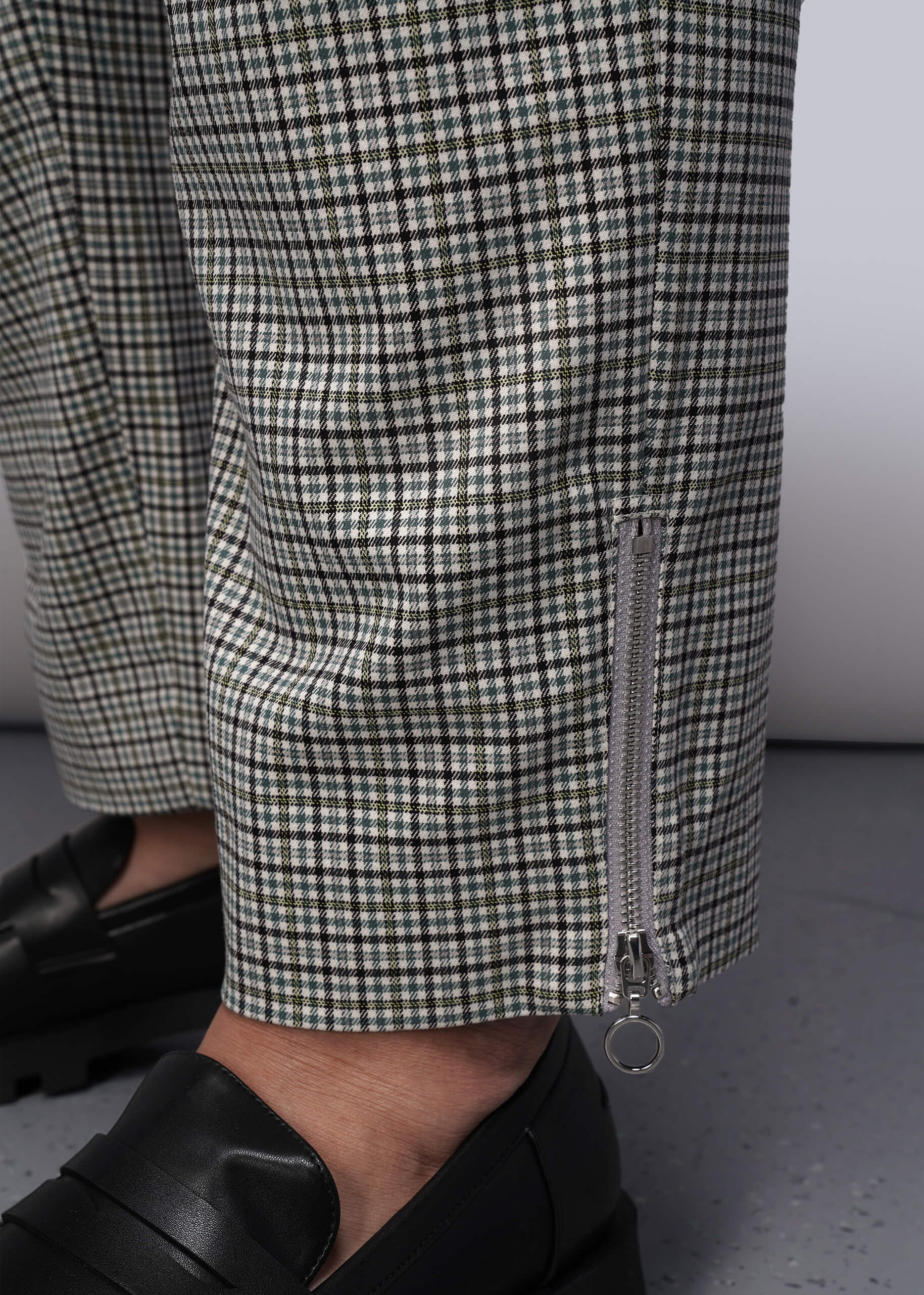 1X=Close-up of a person wearing checkered pants with a zipper detail at hem against a neutral background