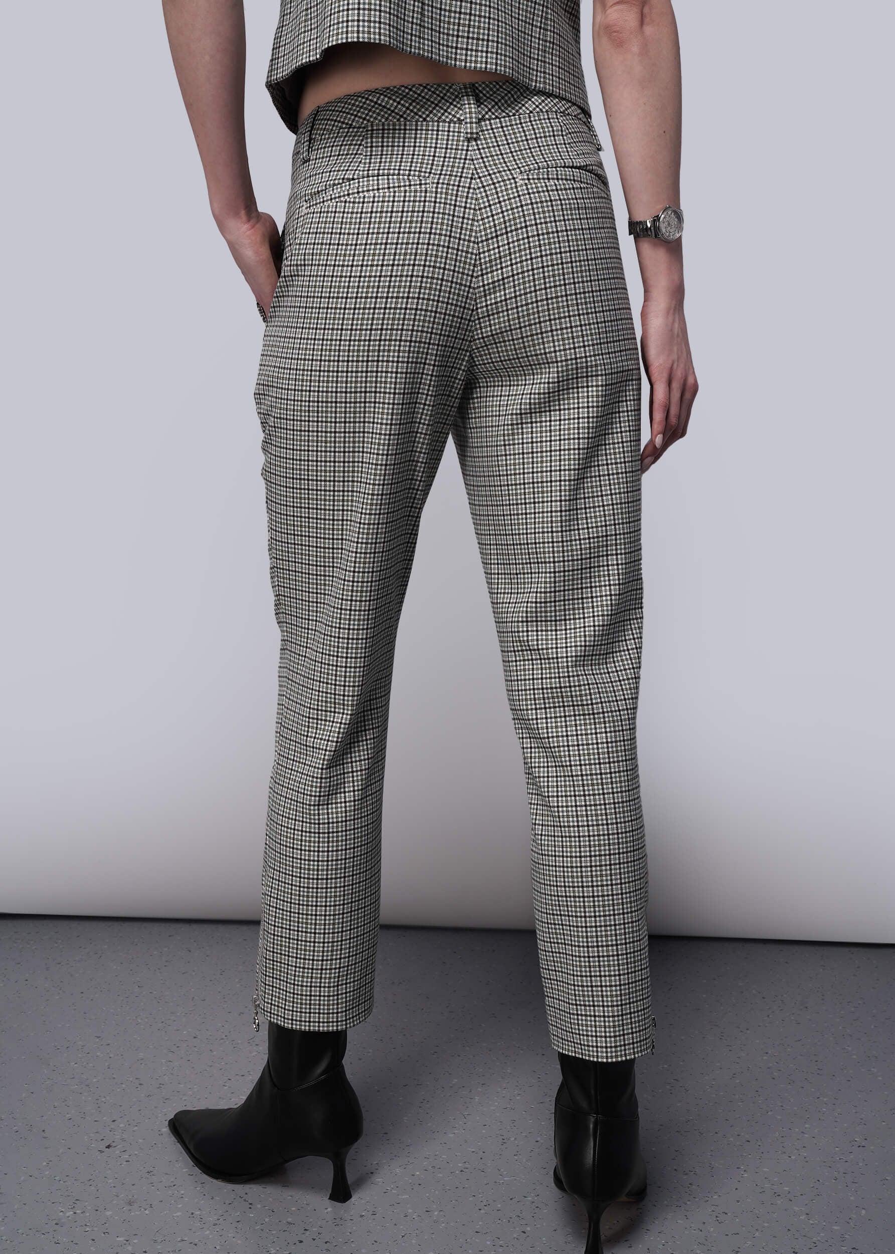 S=Back view of person wearing plaid pants and black boots on a plain background