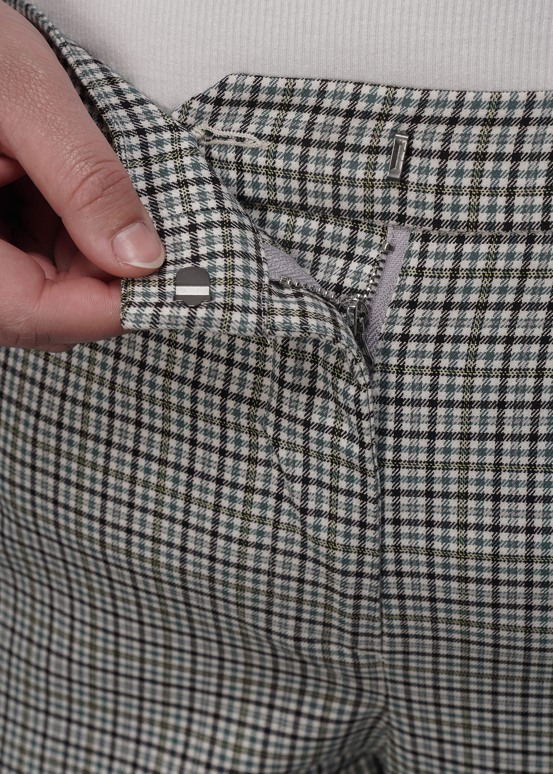 1X=Close-up of a person holding waistband of plaid pants showing button.