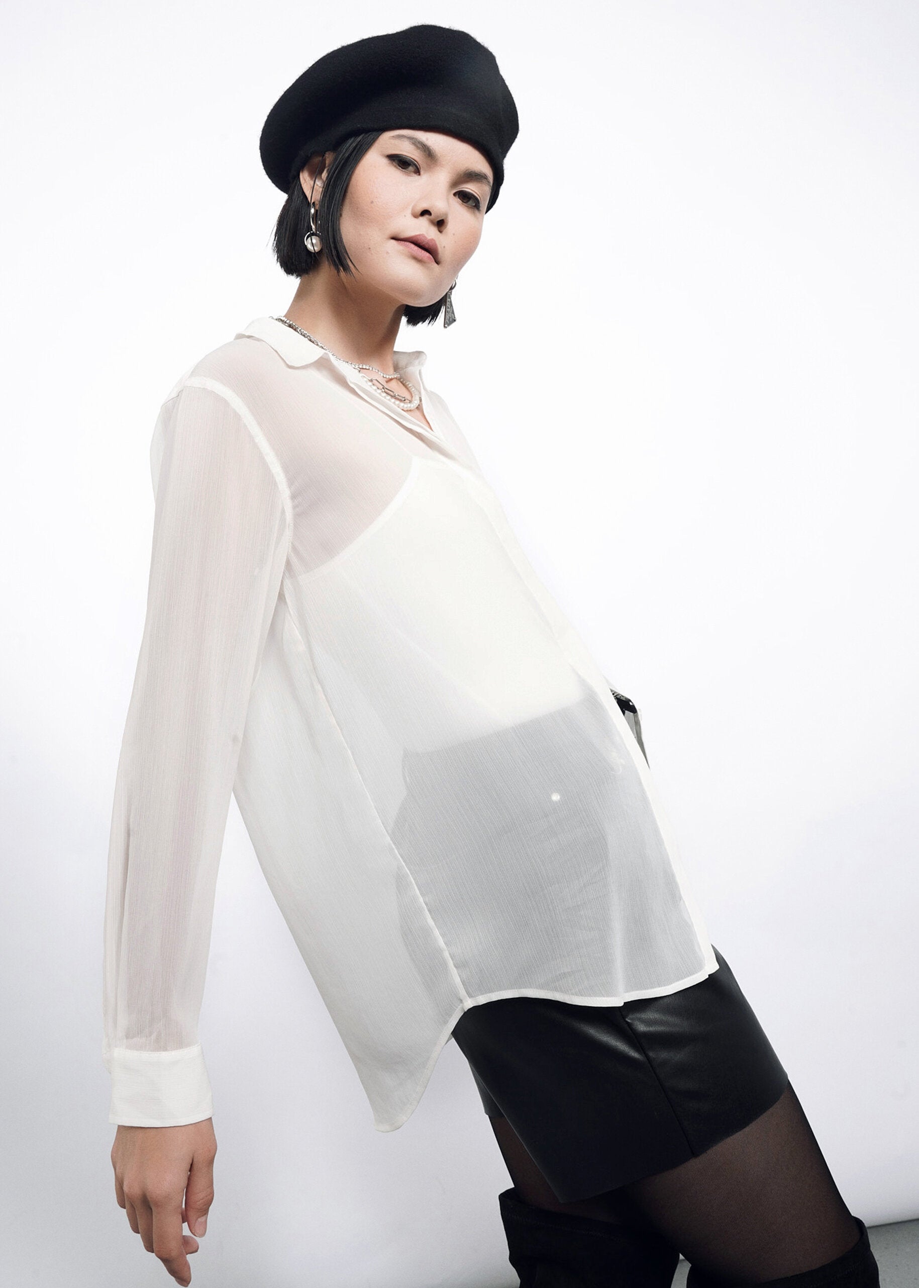 S=A person models The Empower Sheer Long Sleeve Button Up with branded buttons, a black beret, mini skirt, and earrings, posing confidently against a plain white background.