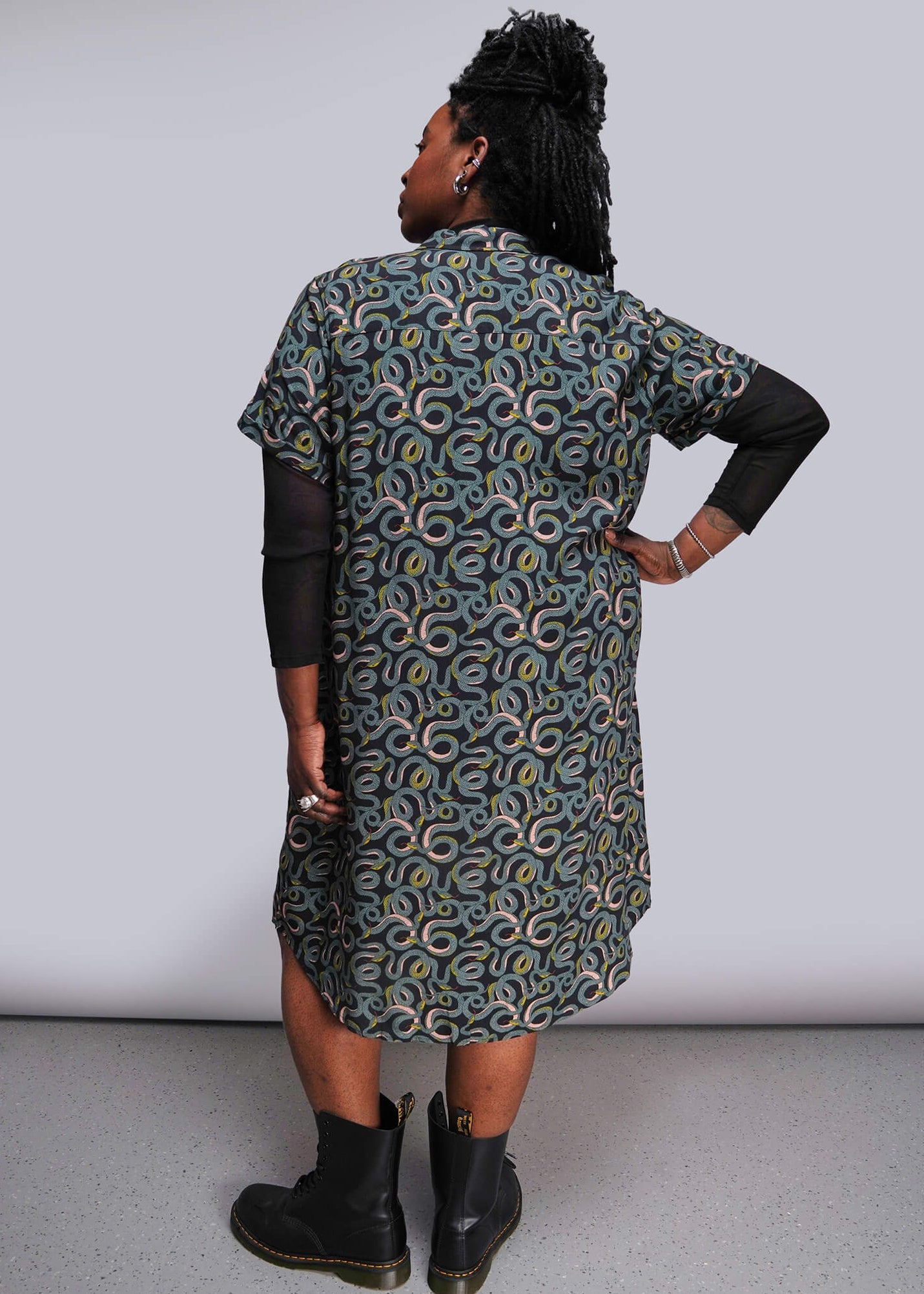 1X=Person wearing a patterned dress with black boots against a plain background